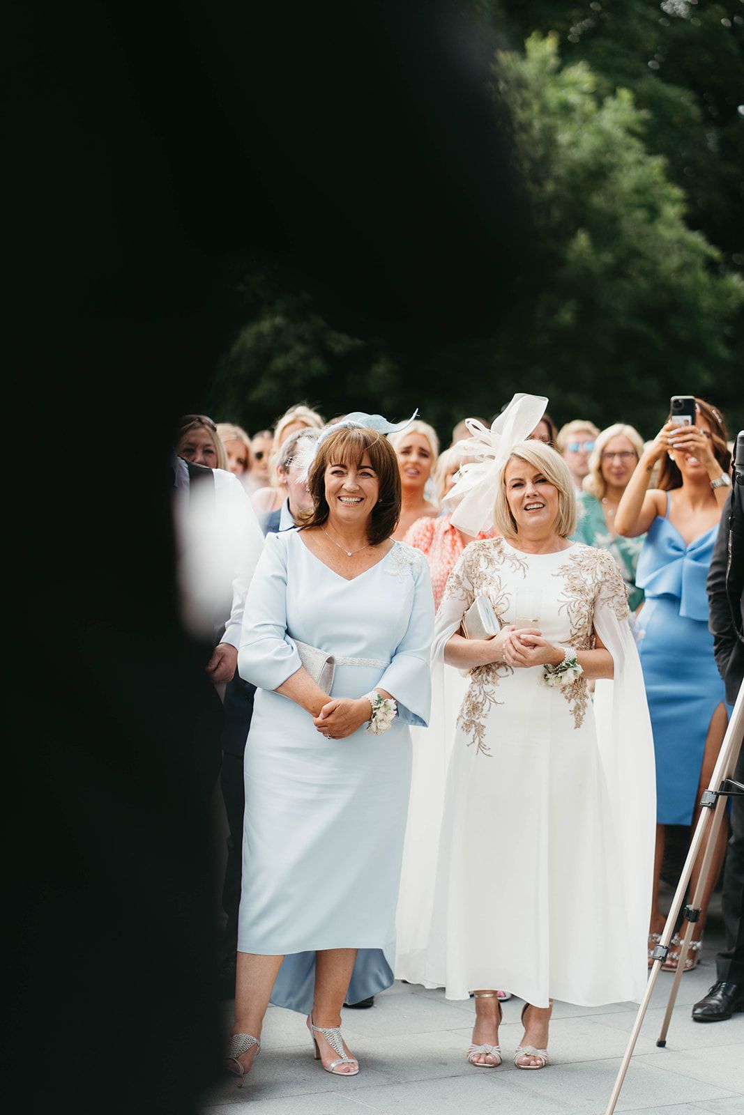 Wedding guests in formal attire gather outdoors for a celebratory moment in pale blue and white dresses.