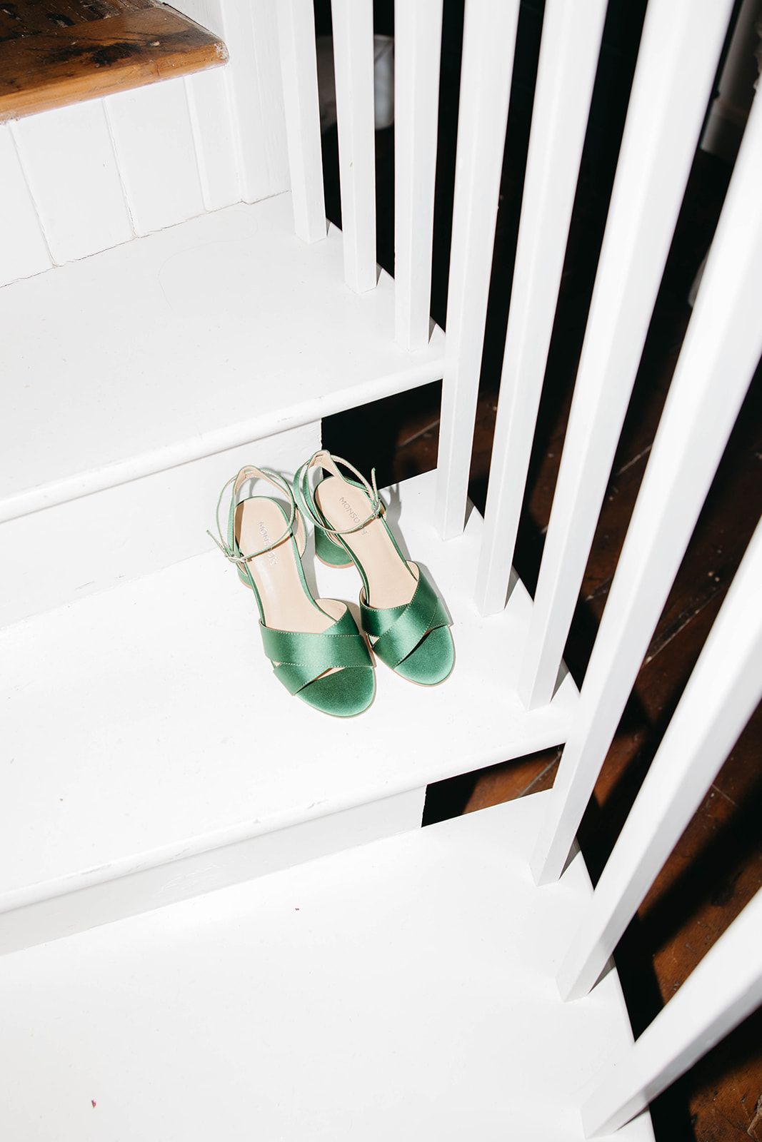 A pair of mint green sandals resting on white wooden stairs with black balusters.