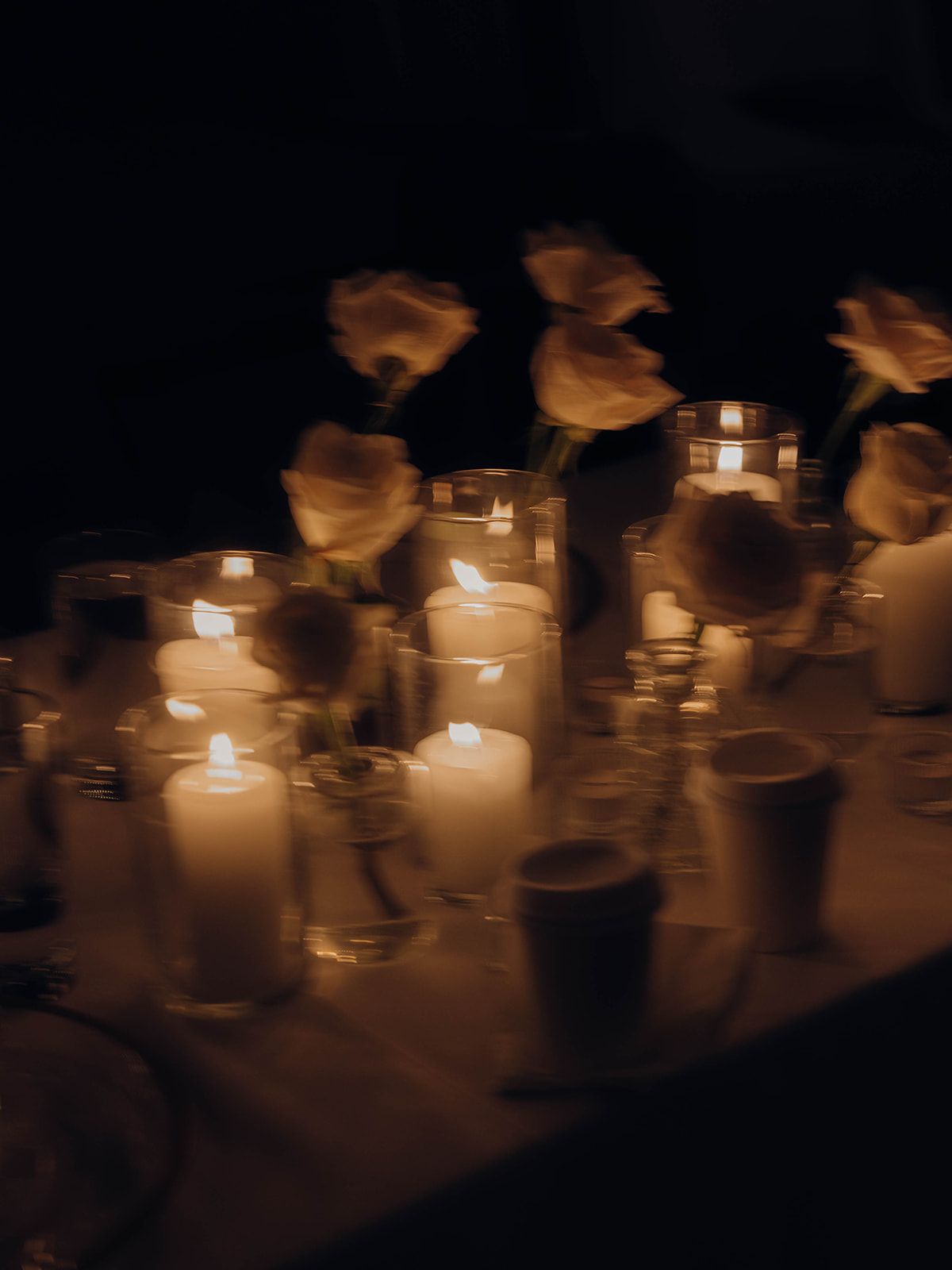 White candles glowing in the darkness with soft orange roses creating a romantic and somber atmosphere.