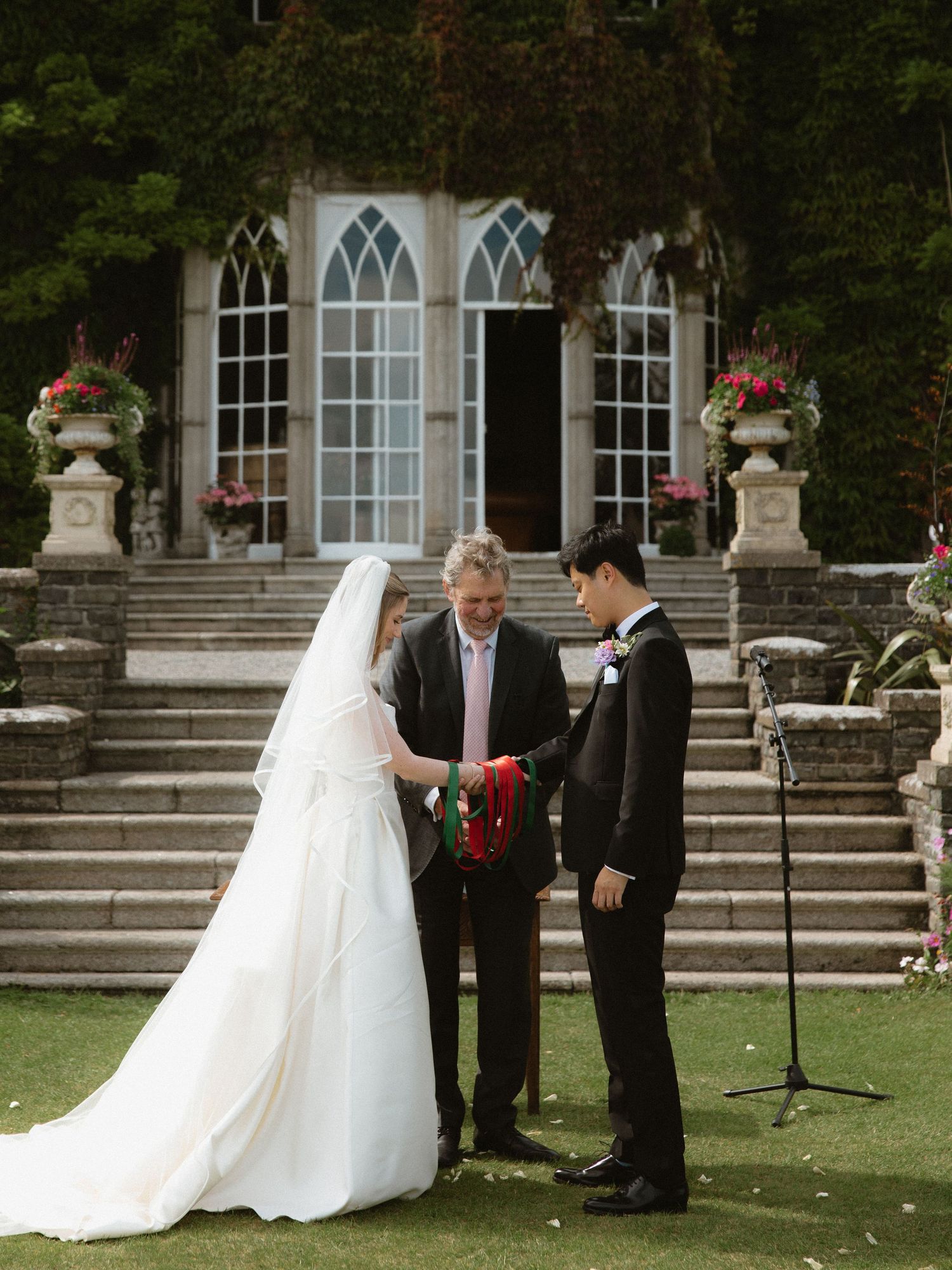 Wedding ceremony taking place on stone steps of a Gothic-style building with arched windows.