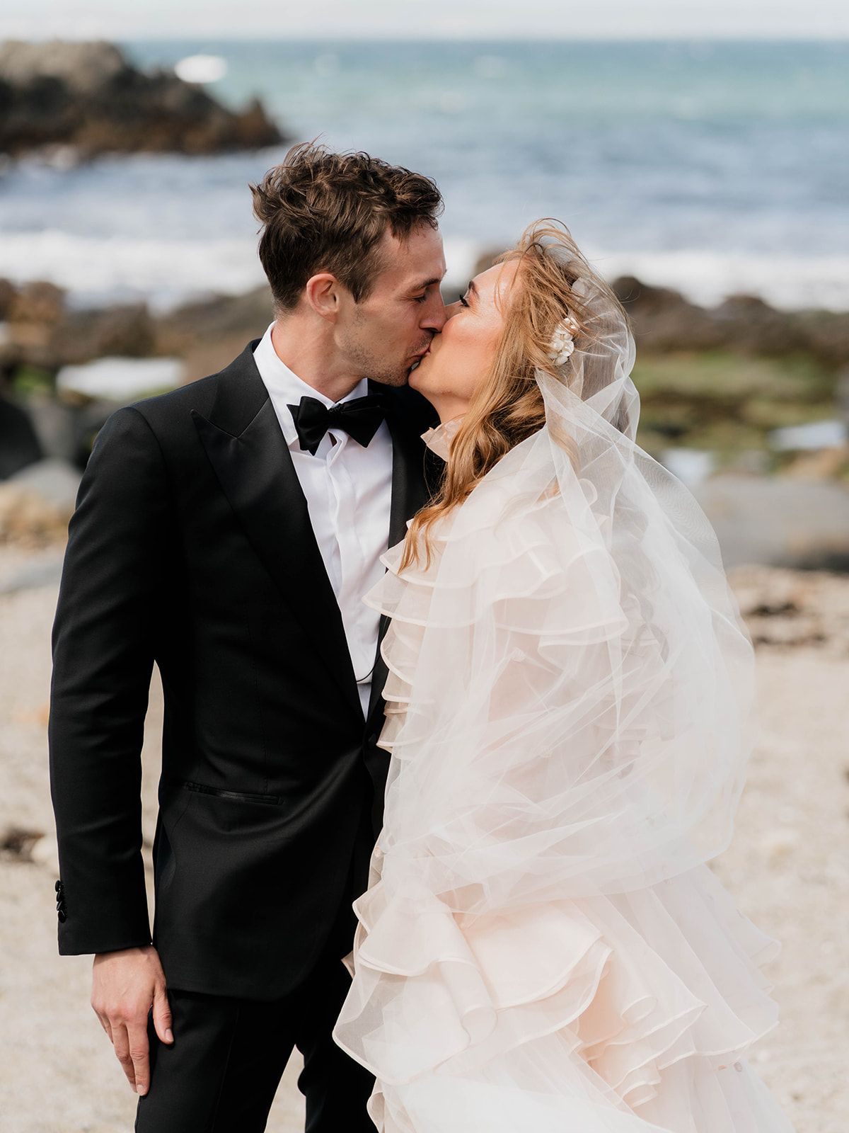 Romantic beachside wedding portrait with ocean and rocky coast in background.