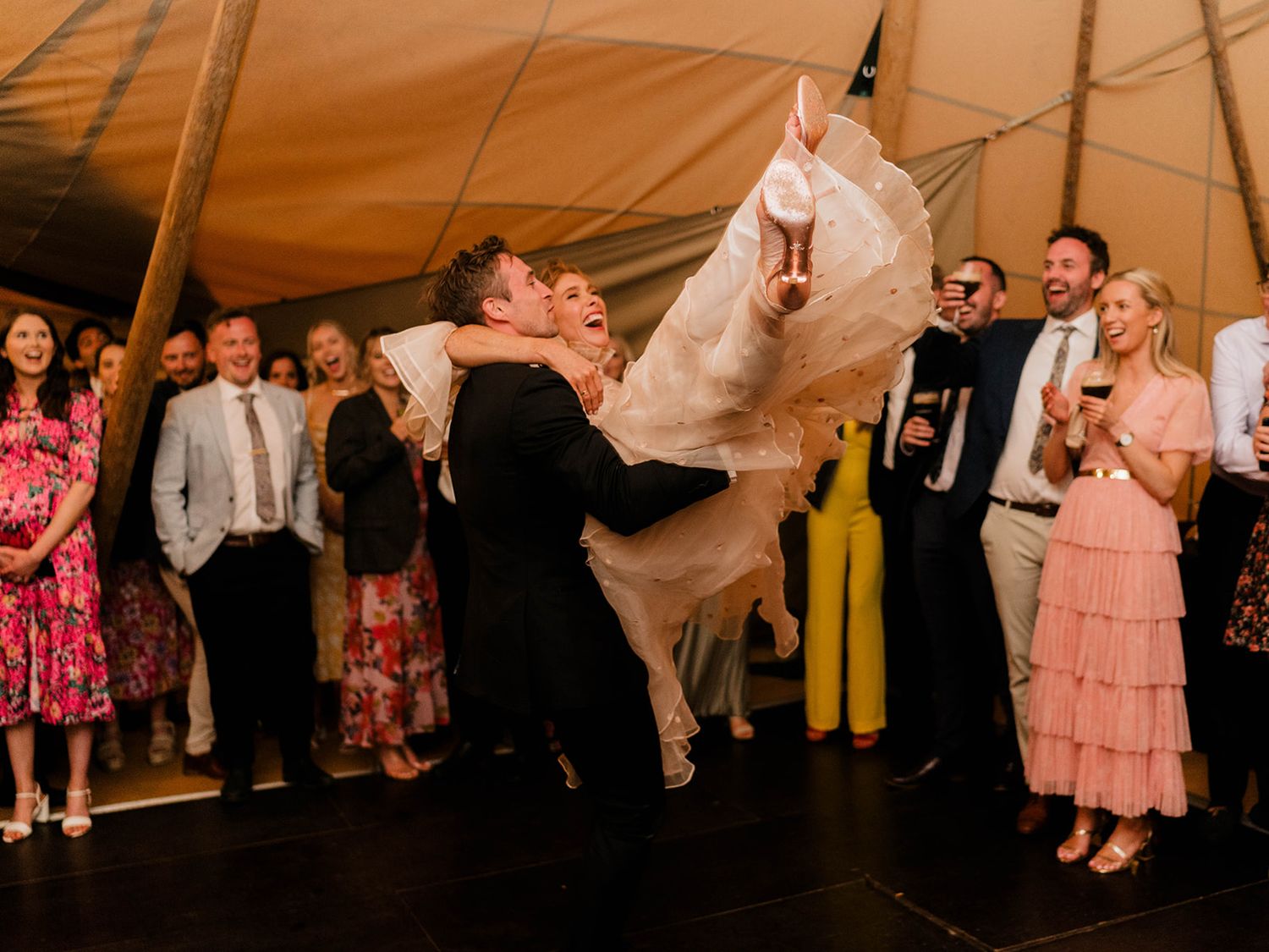 Wedding couple performs dramatic dance lift surrounded by guests in a tented reception.