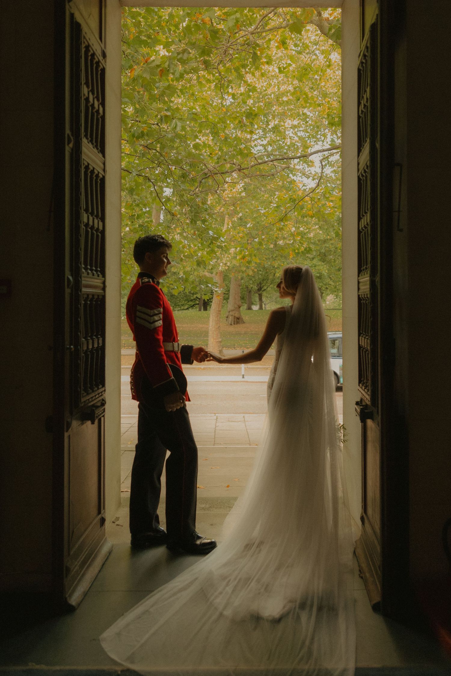 Silhouette of a bride and groom standing in a church doorway with sunlit trees visible in the background.