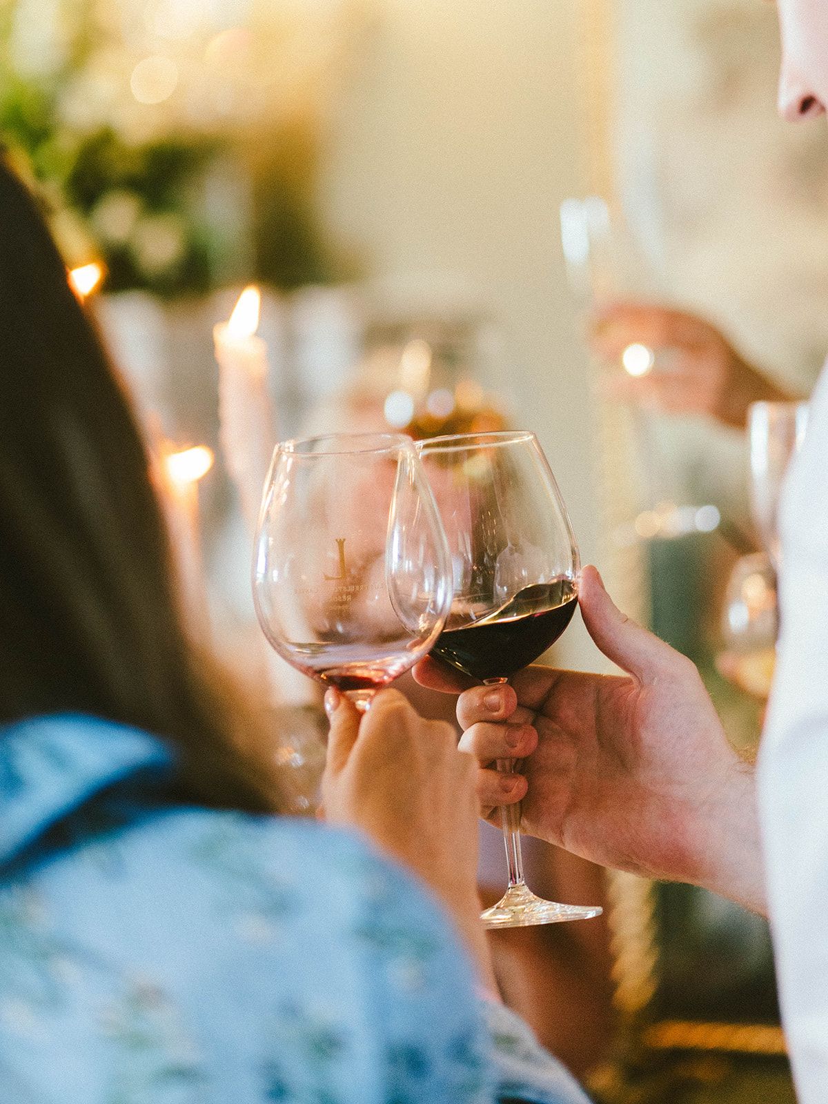 People toasting with red wine glasses at a candlelit dinner celebration.