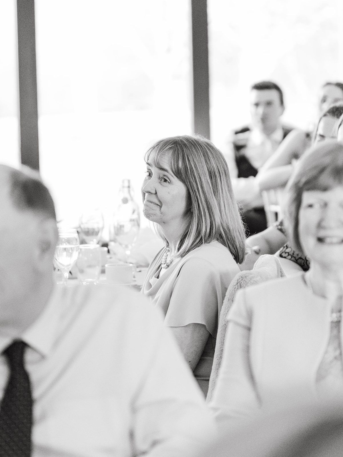 Black and white photo of guests seated at a formal dining event with large windows in the background.