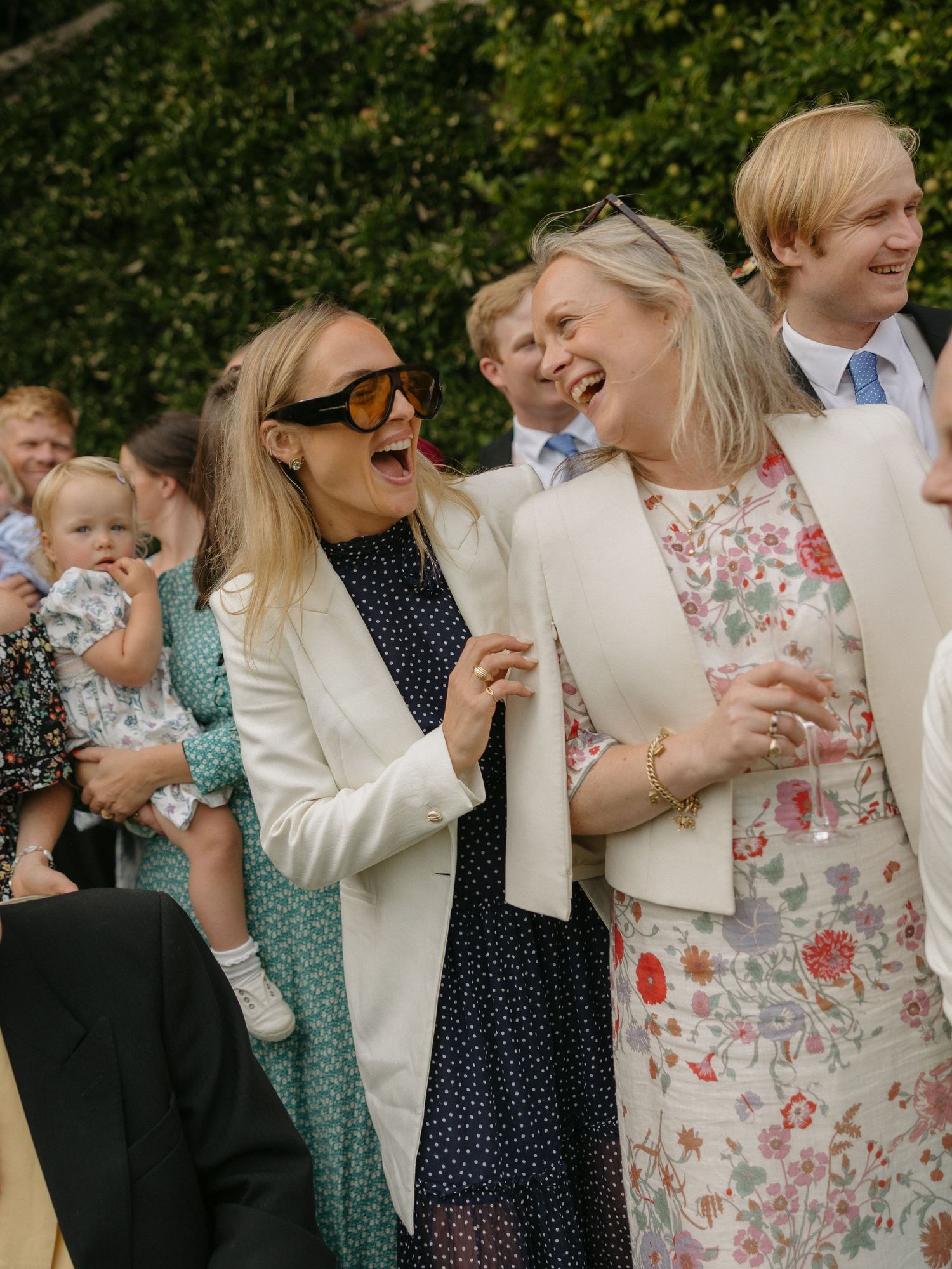 A joyful group sharing laughter at an outdoor celebration wearing elegant spring attire.