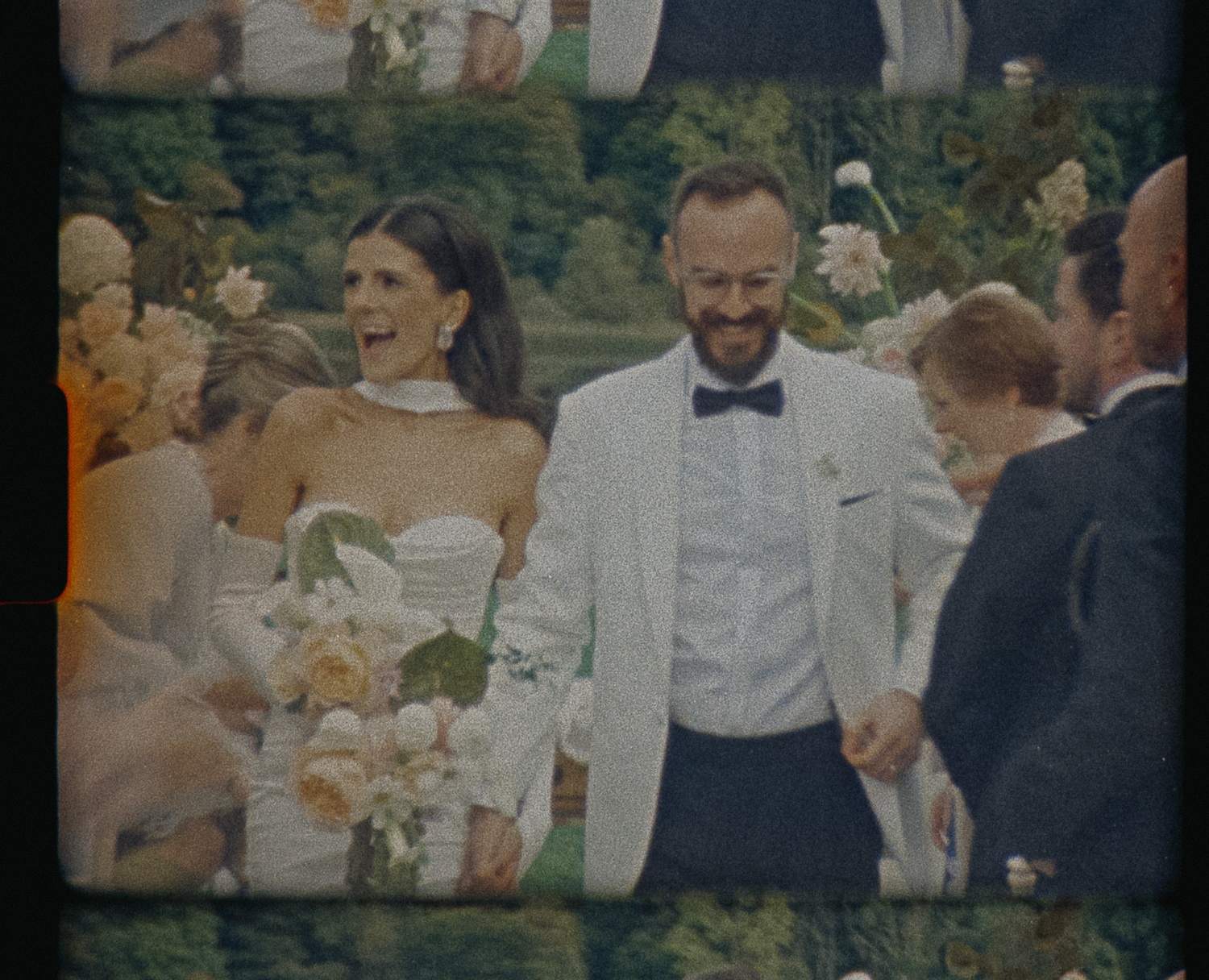 A group of wedding guests gather outdoors for a celebration with formal attire and floral decorations.