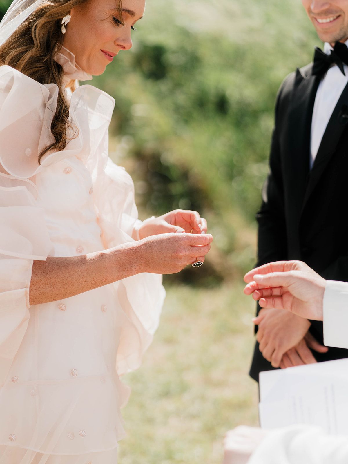 Close-up of hands exchanging wedding rings during an outdoor ceremony.
