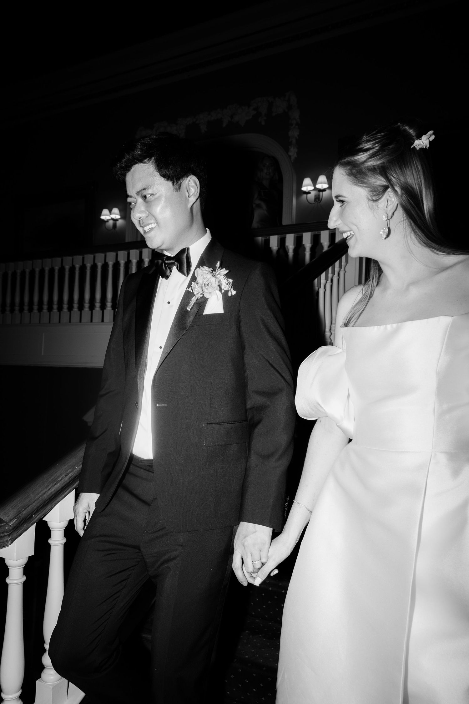 A couple descends a grand staircase during their black-tie wedding celebration.