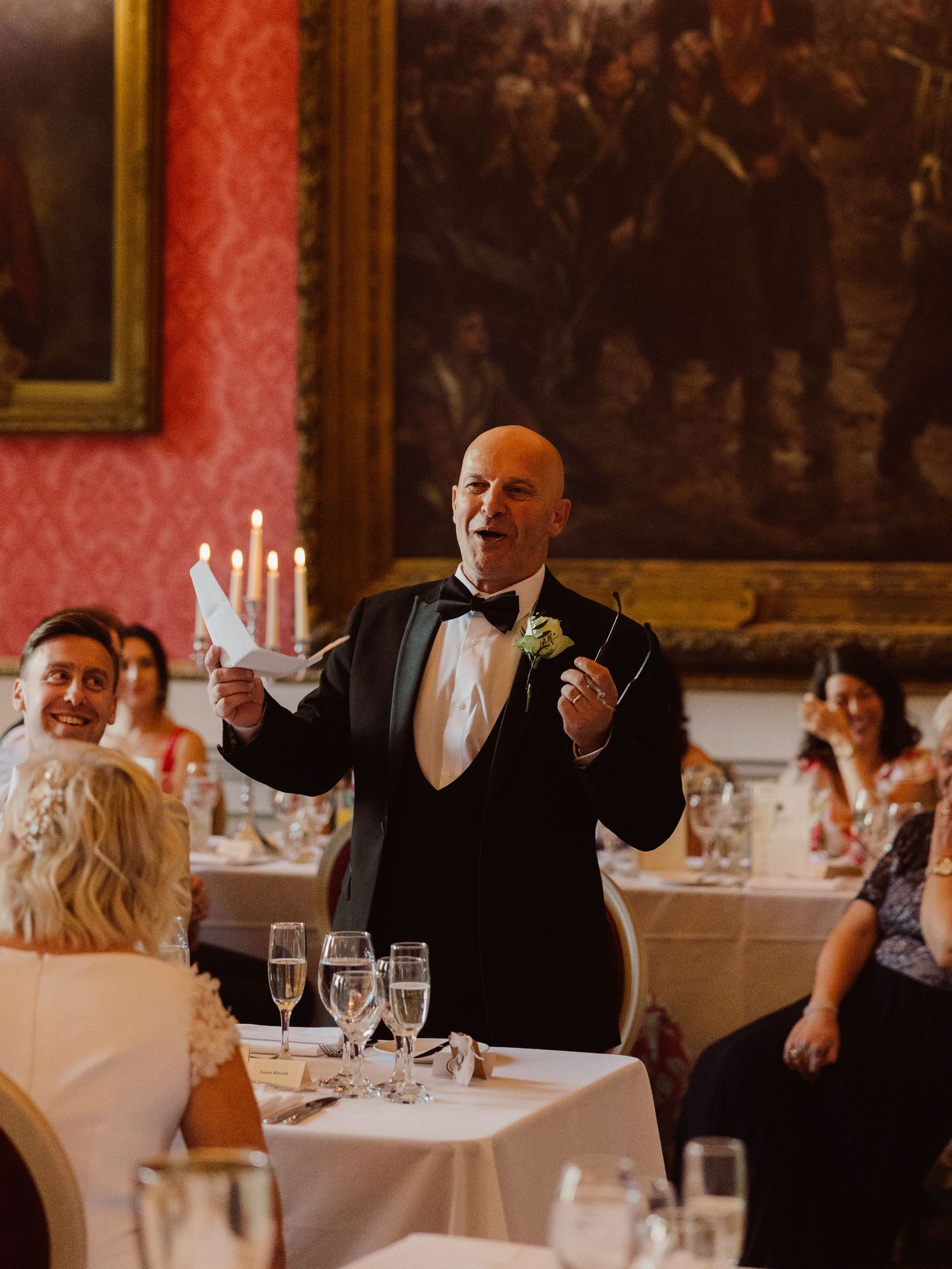 Wedding guests enjoying a candlelit dinner reception in an elegant dining room with red walls and white tablecloths.