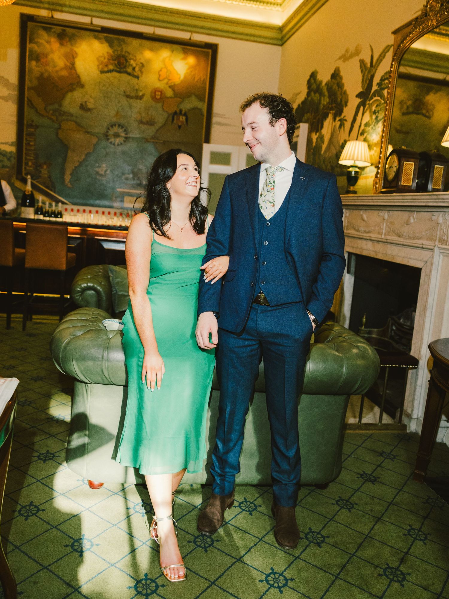 A couple in blue suit and green dress share playful moments across a series of photos in an elegant interior space.