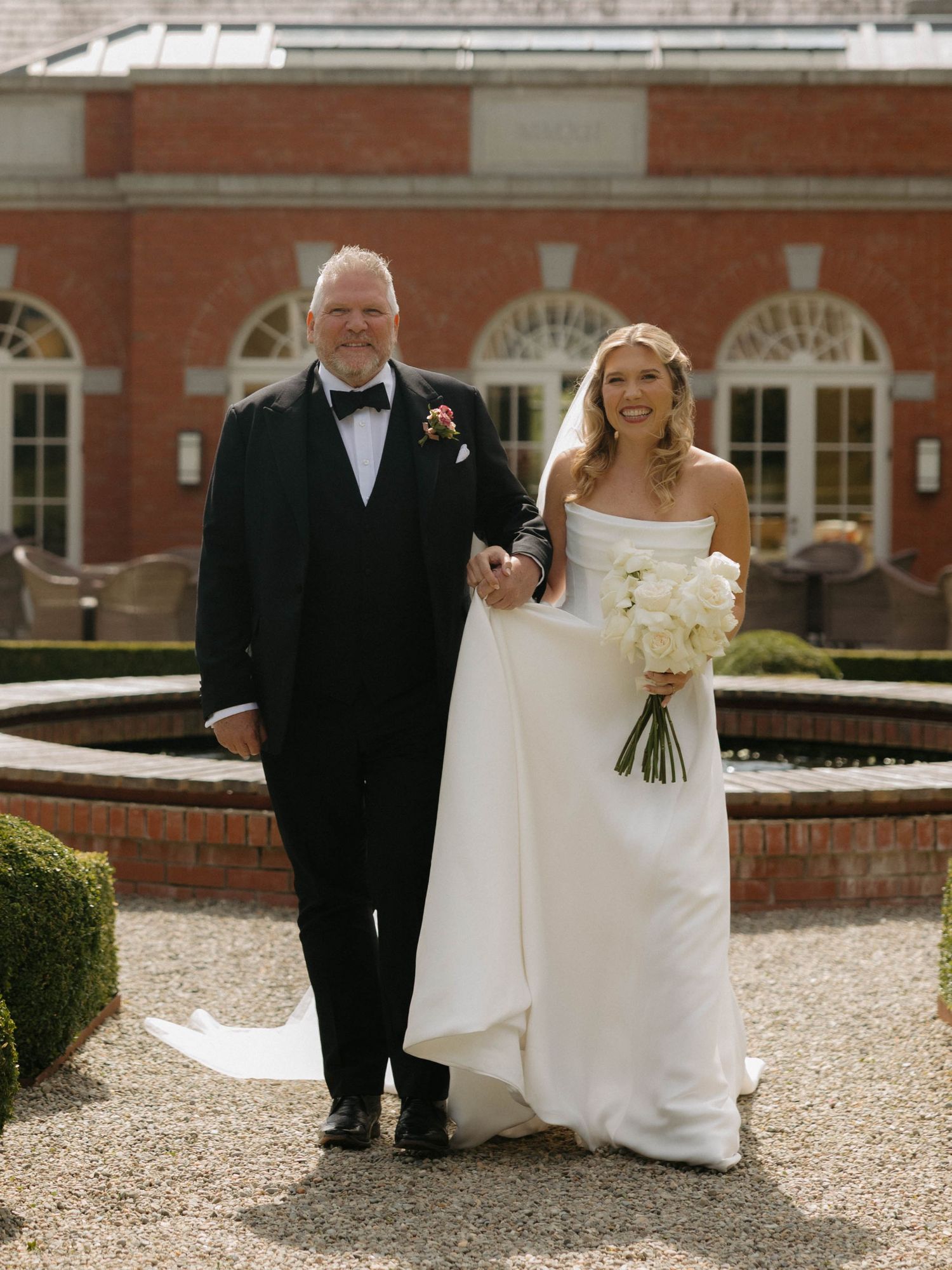 Elegant wedding portrait on a gravel path in front of a historic brick building.