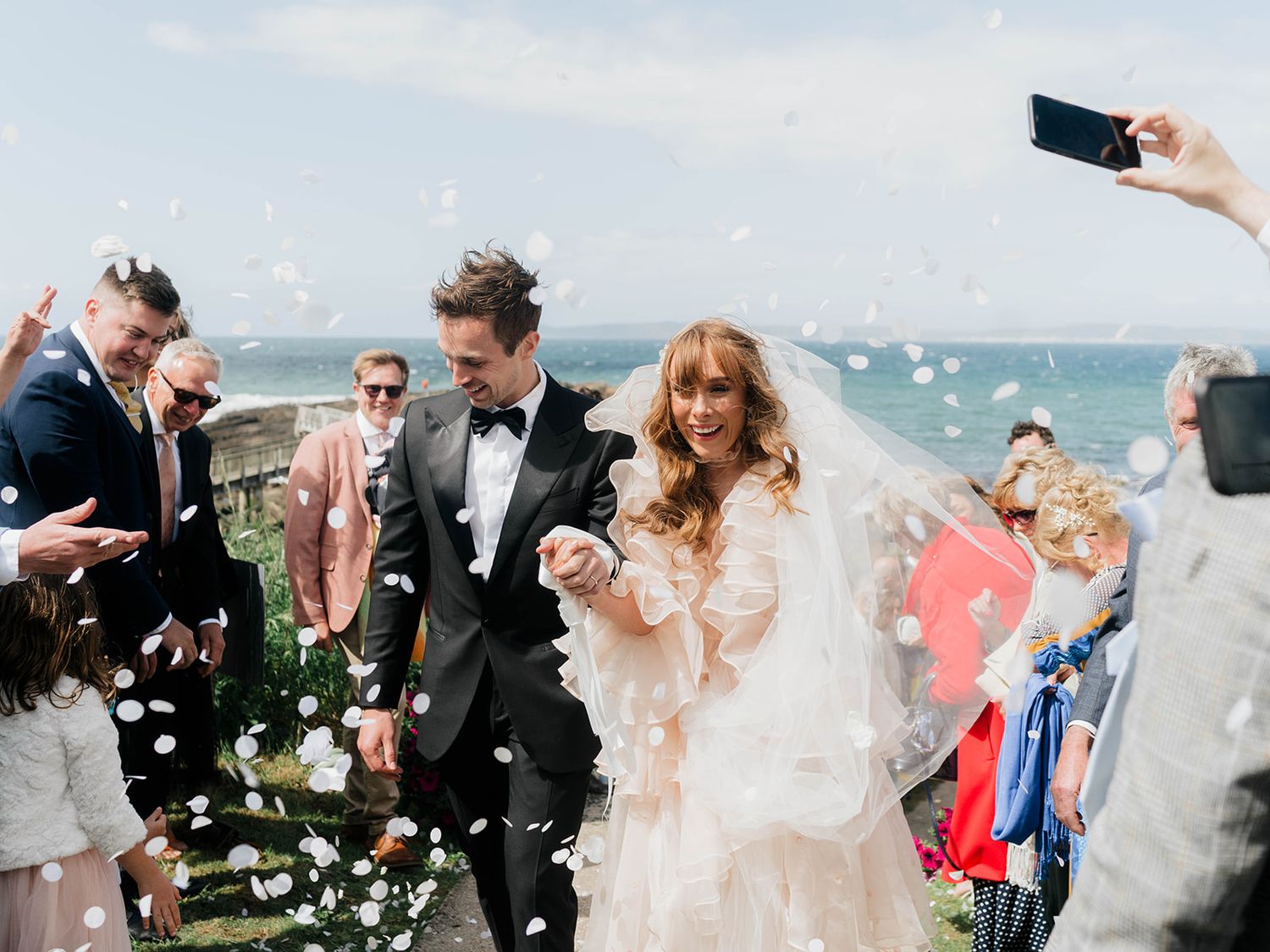 Newlyweds walking through shower of bubbles during seaside celebration.