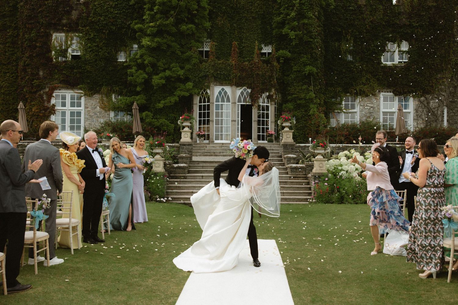 Wedding celebration with guests tossing confetti as couple dances on white runner.