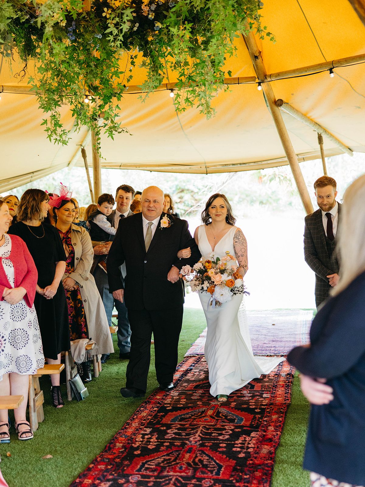 Wedding ceremony under a white tent with a decorative red Persian runner and greenery hanging from above.