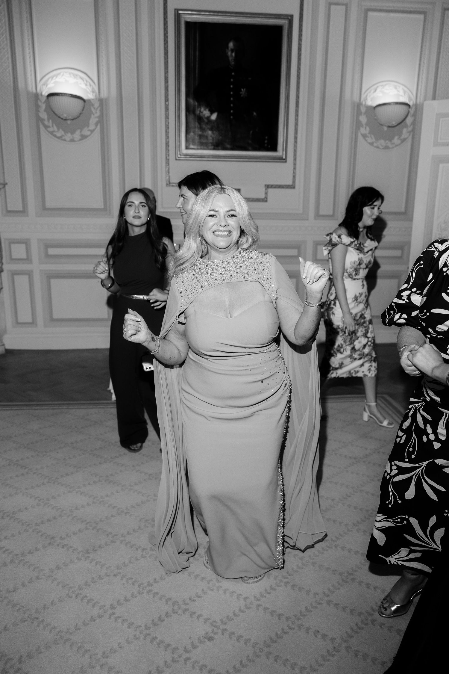 At a joyful dance event, elderly guests move across an elegant ballroom with patterned carpet and white walls.