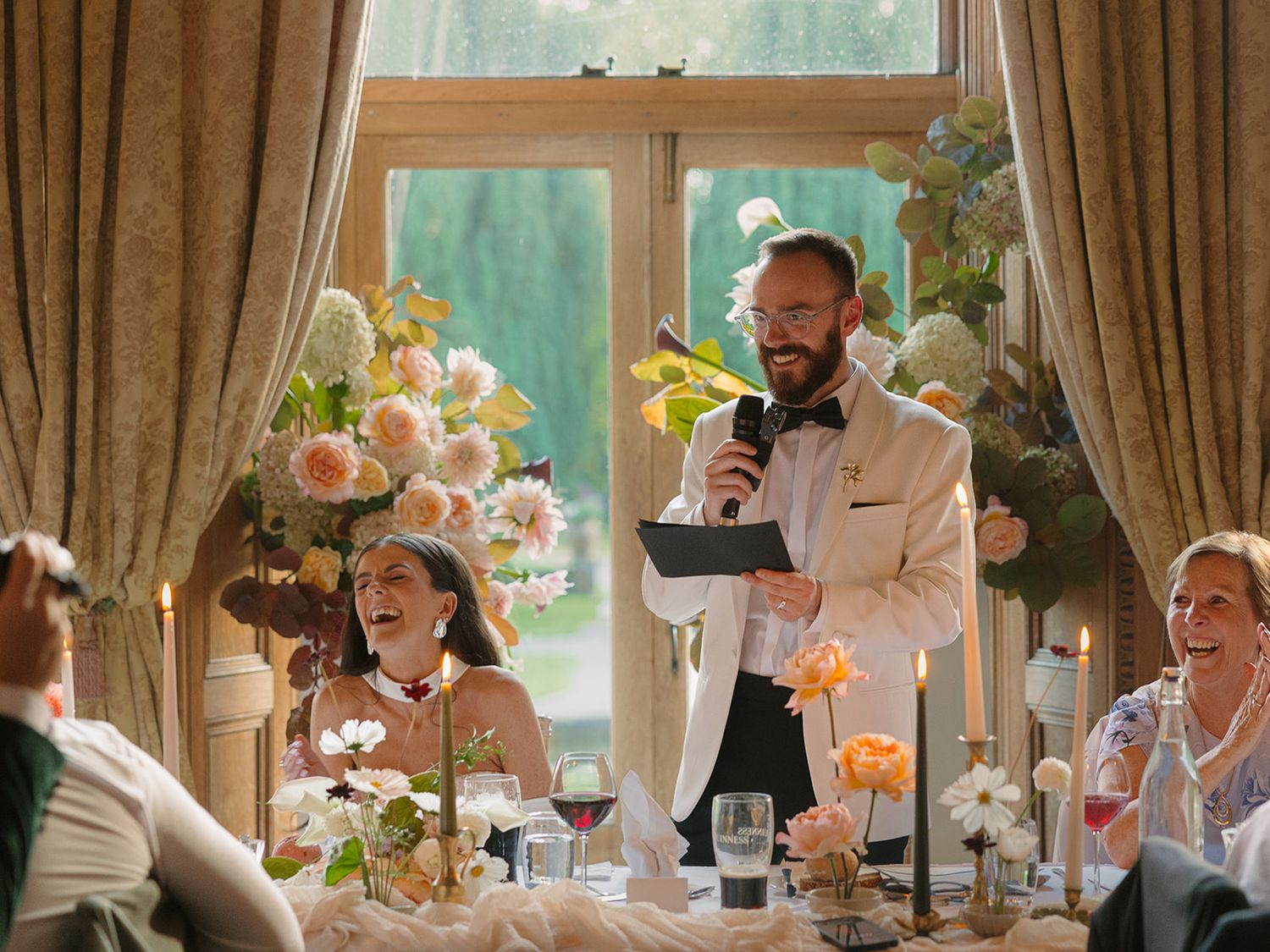 A lively banquet scene shows people raising their glasses in a toast at an elegant dining room with brown curtains.