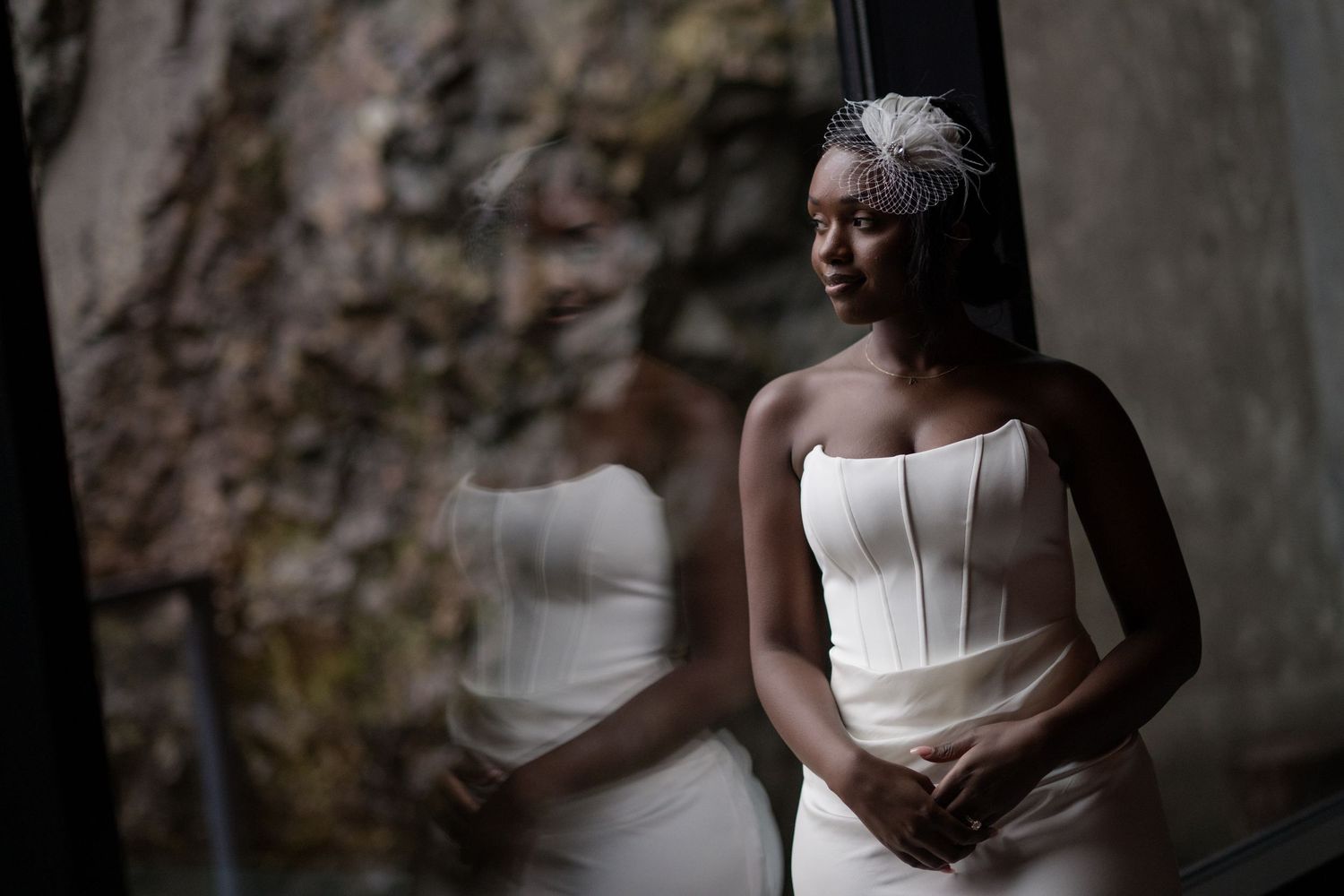 A bride in a white strapless wedding dress poses against a rustic stone wall background.