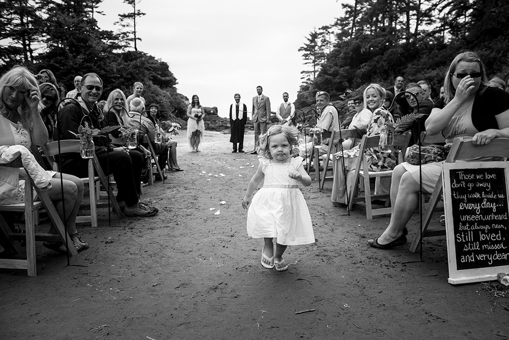 Rustic outdoor wedding ceremony setup with wooden chairs and chalkboard signs on a beach path.