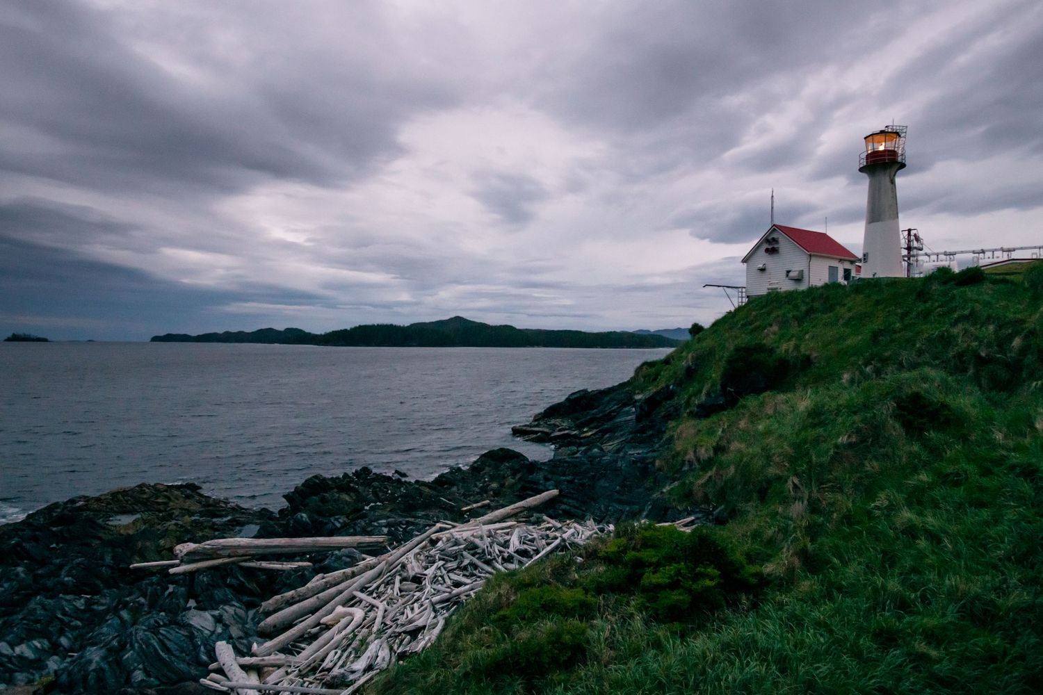 Dramatic coastal lighthouse perched on rocky cliffs overlooking a moody ocean under stormy skies.