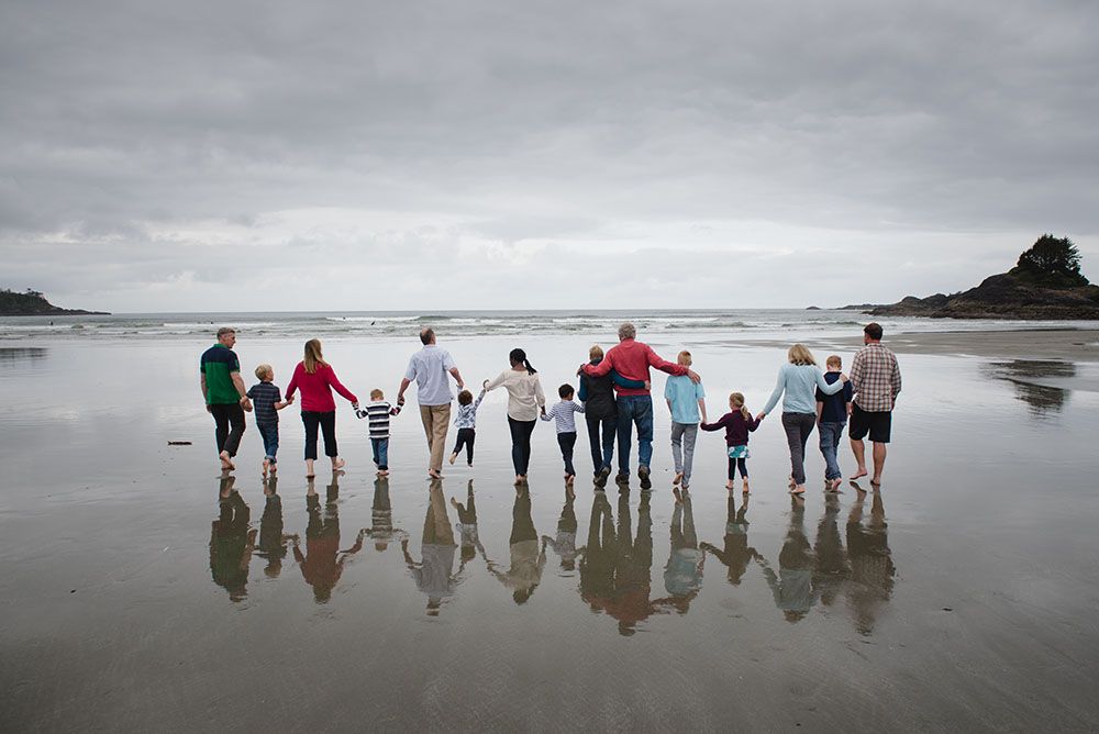 A group of people holding hands while standing in a line at the beach with their reflection visible in the wet sand.