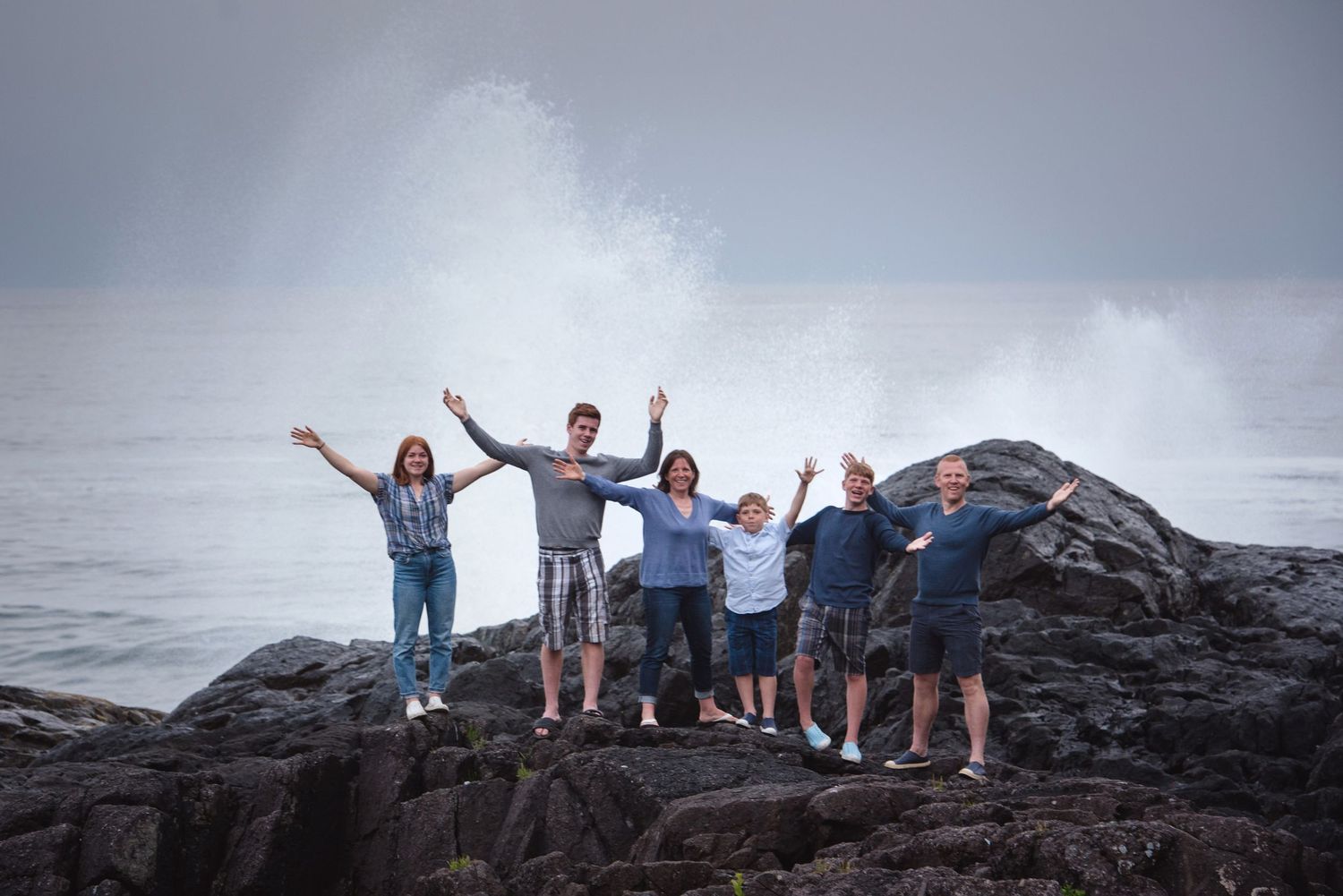 People posing on rocky coastal formations with waves and cloudy skies in the background.
