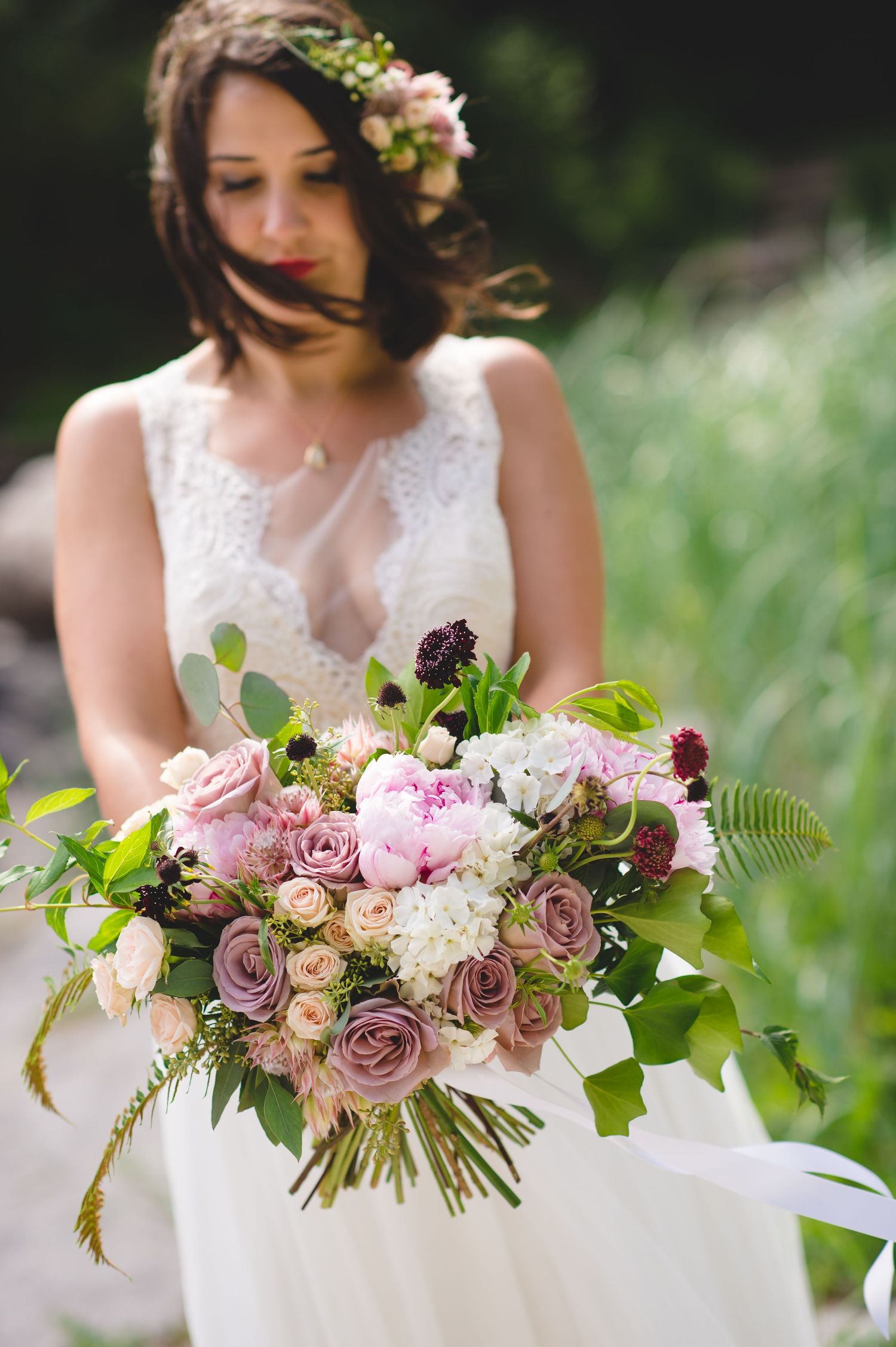 Elegant bridal bouquet with dusty rose flowers and fresh greenery in natural outdoor setting.