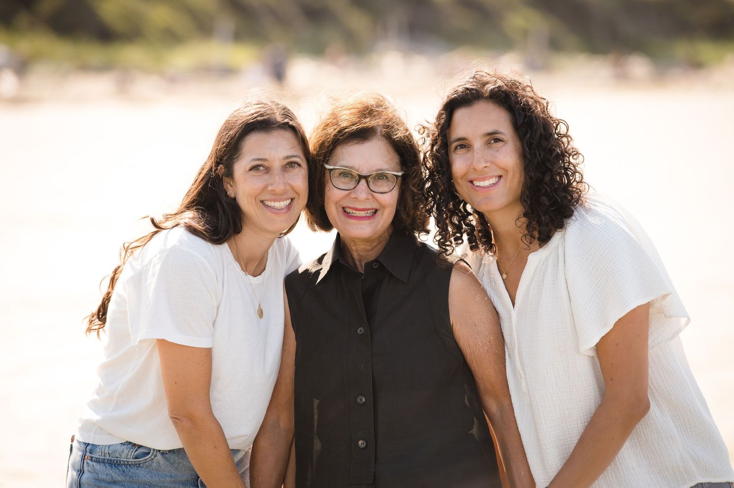 Three people smiling together in warm sunlight against a beach backdrop.