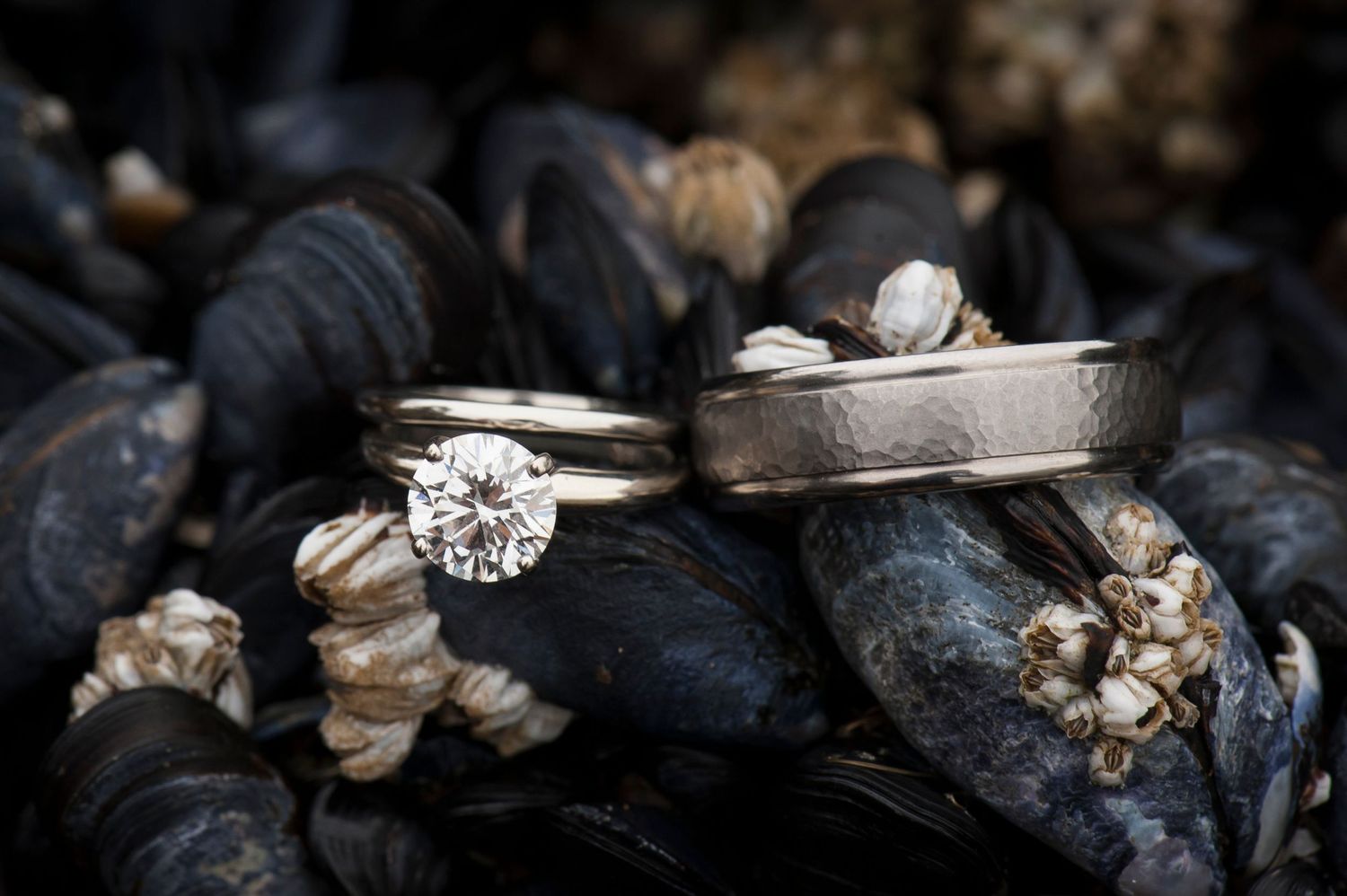 Close-up of diamond engagement ring and wedding bands on dark stones.