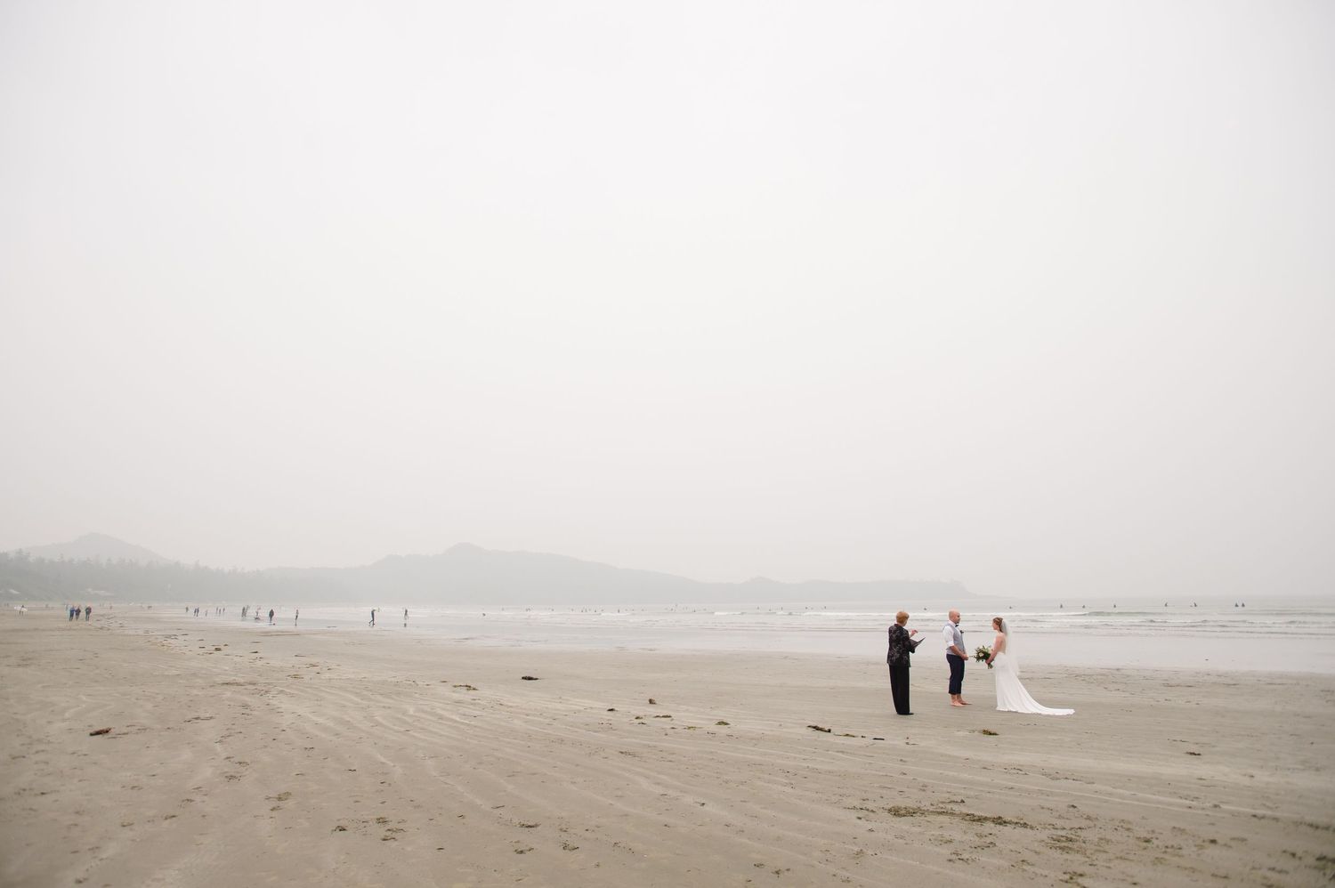 Silhouettes of people walking on a misty beach with waves rolling in on a cloudy day.