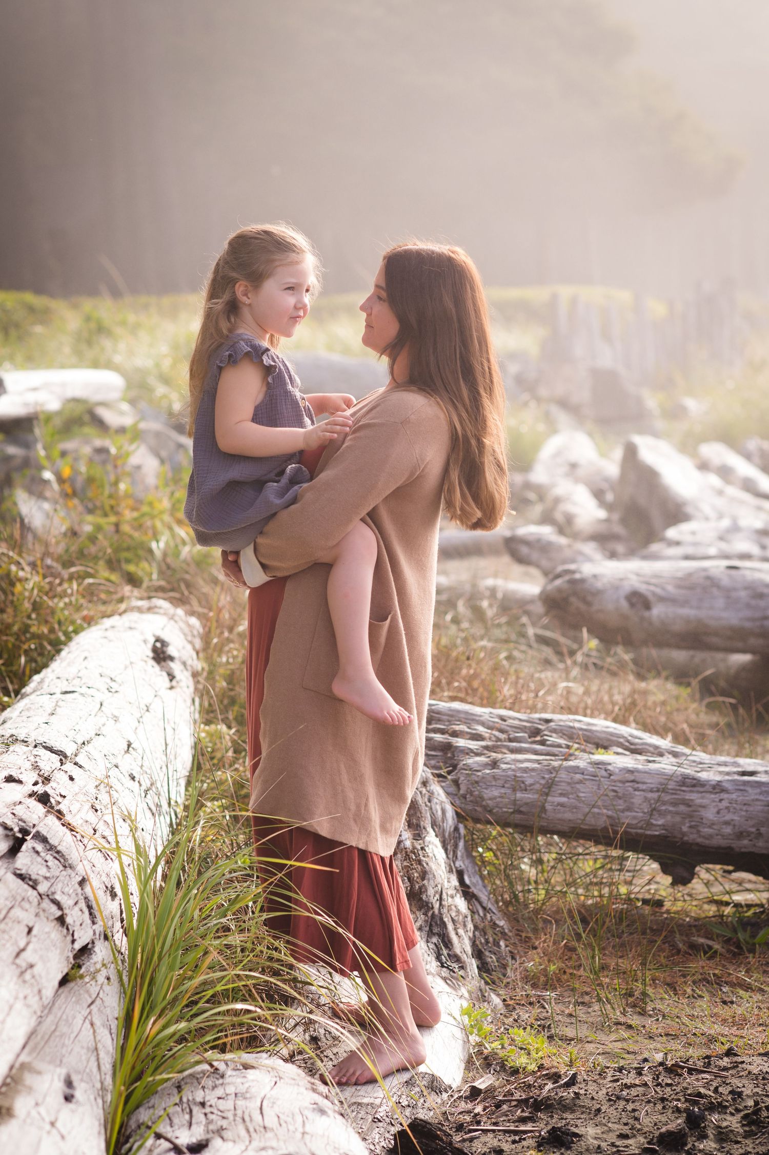 Two people share an intimate moment while standing on driftwood at the beach.