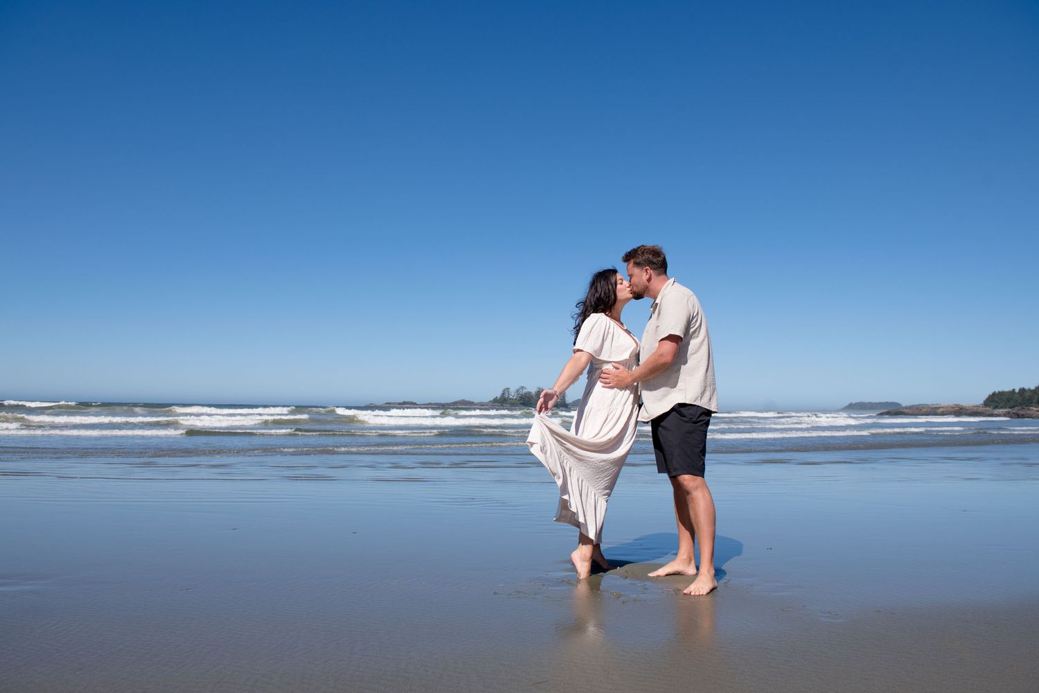 Romantic maternity photos captured on a sunny beach with crashing waves.