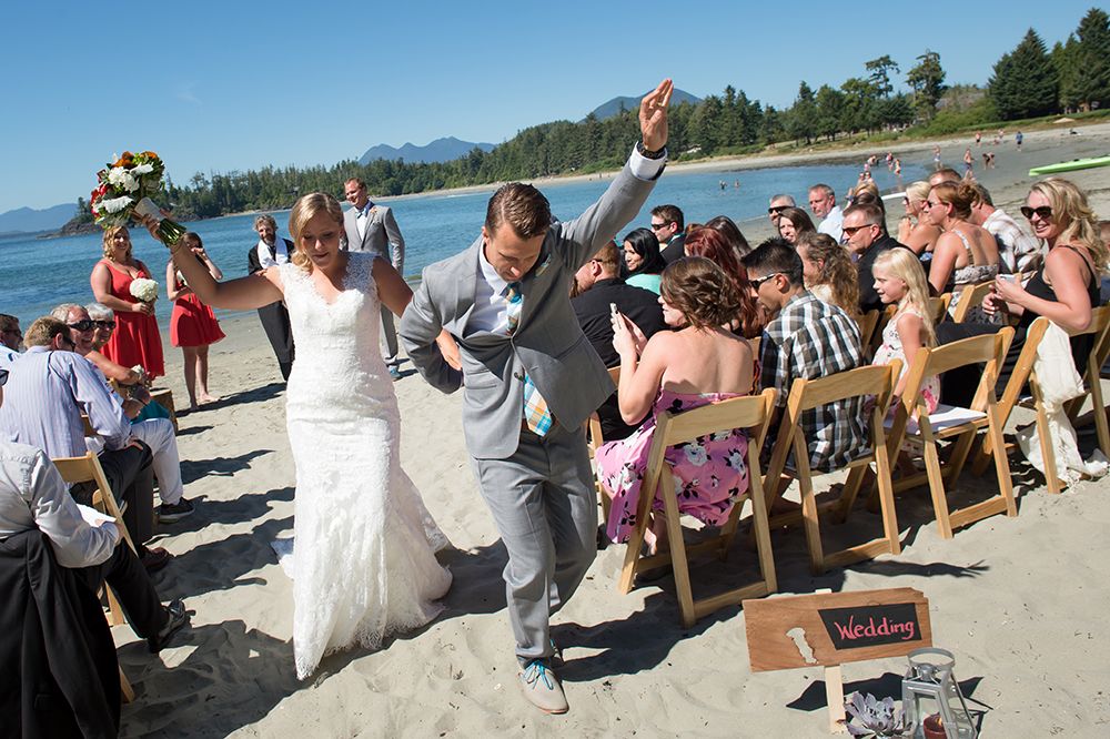 Beach wedding ceremony with guests seated on wooden chairs along the shoreline.