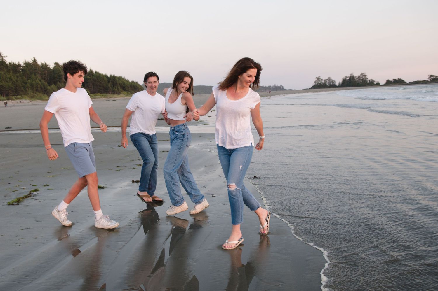 Family walking together along the beach shoreline at sunset creating silhouettes against the water.