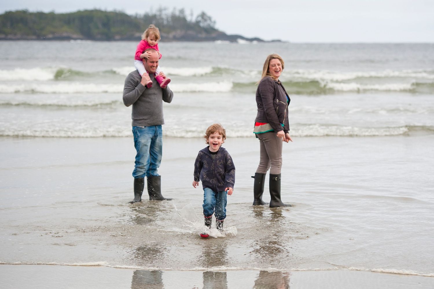 People wading in shallow ocean waves along a misty Pacific Northwest beach.