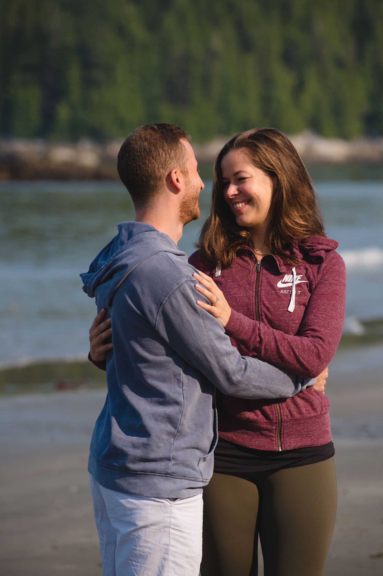 A couple shares an intimate moment together on a beach with water and trees in the background.