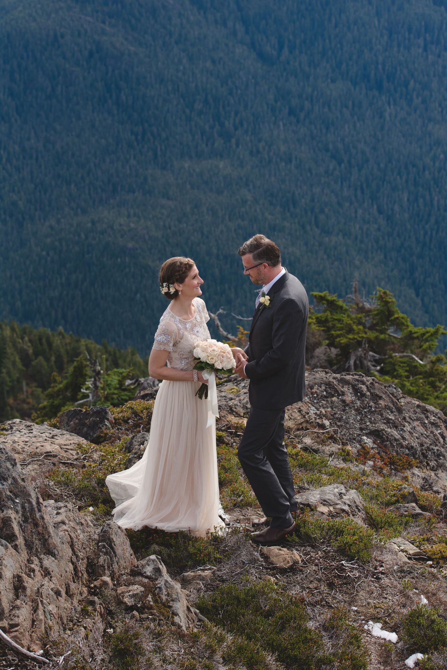 A couple exchanges wedding vows on a rocky mountain overlook surrounded by forest views.