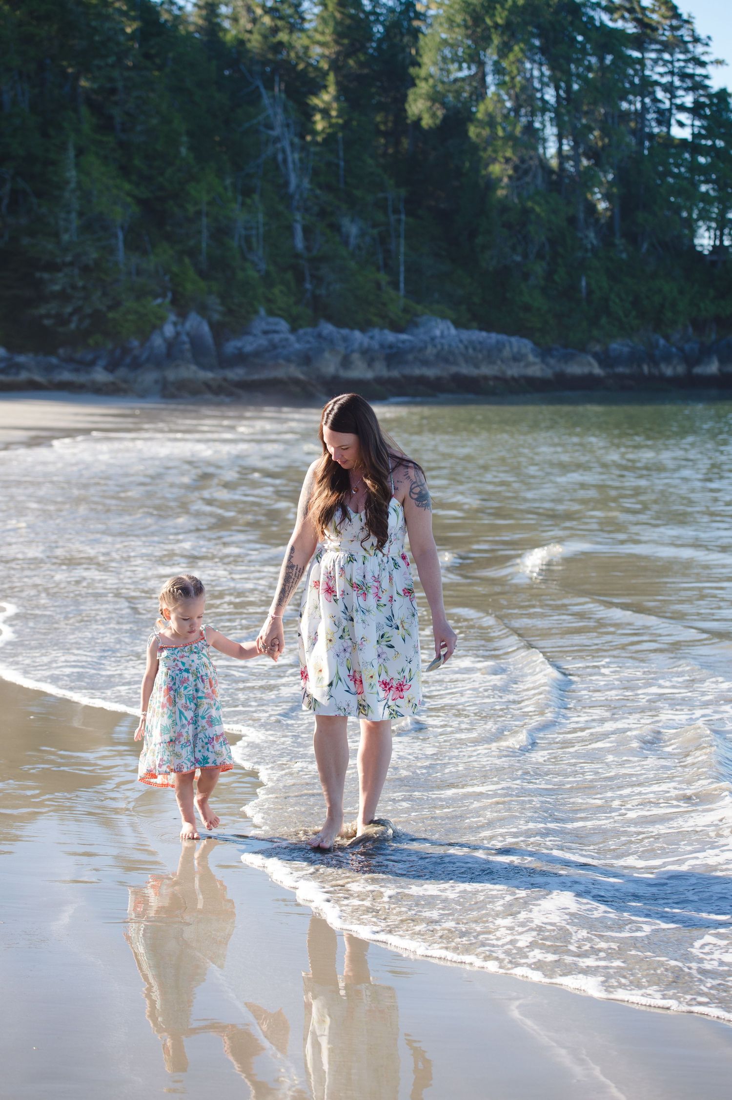 Beachgoers enjoying waves and sand along forested coastline on sunny afternoon.