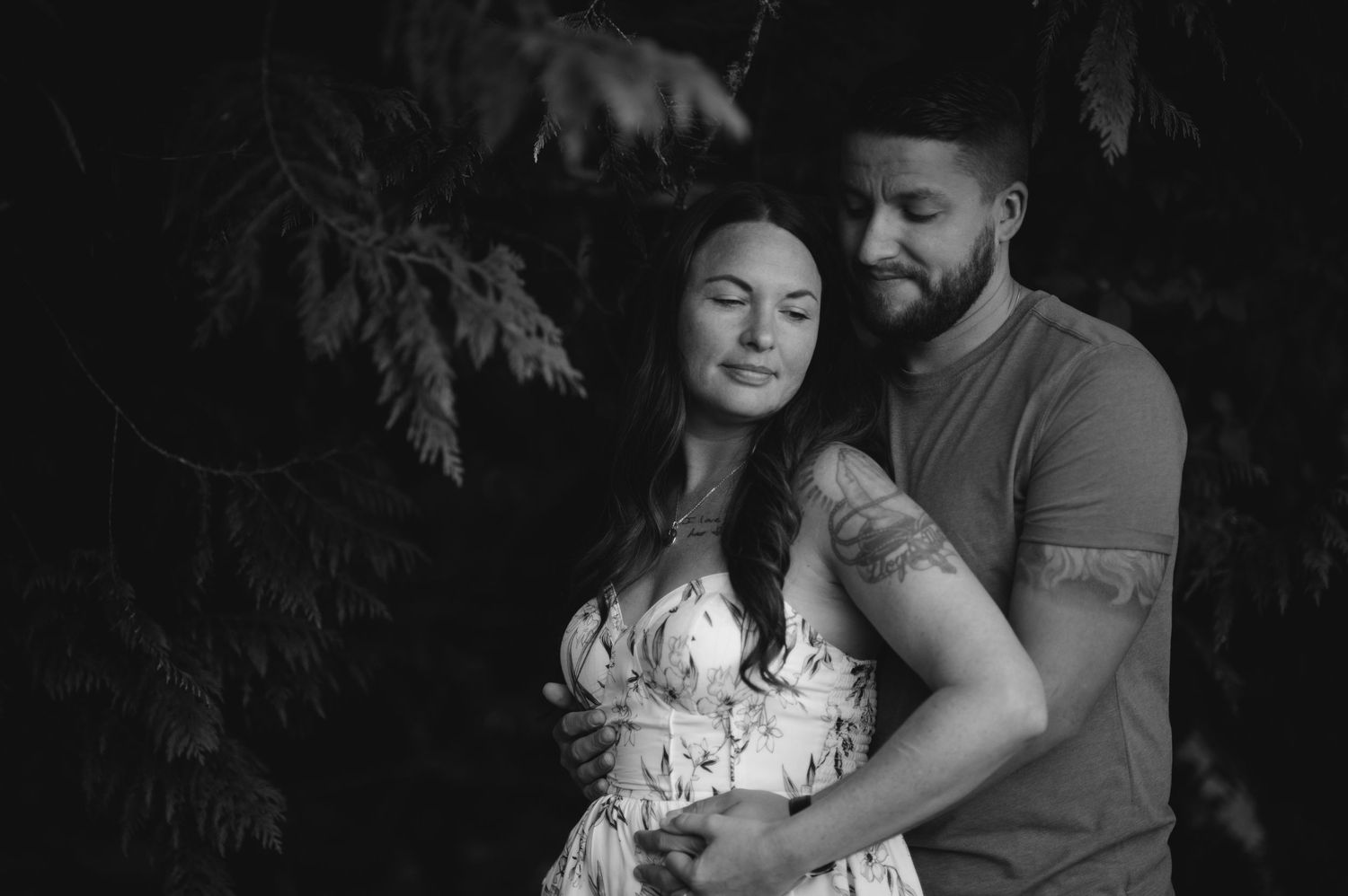 A couple shares an intimate moment while standing among evergreen trees.