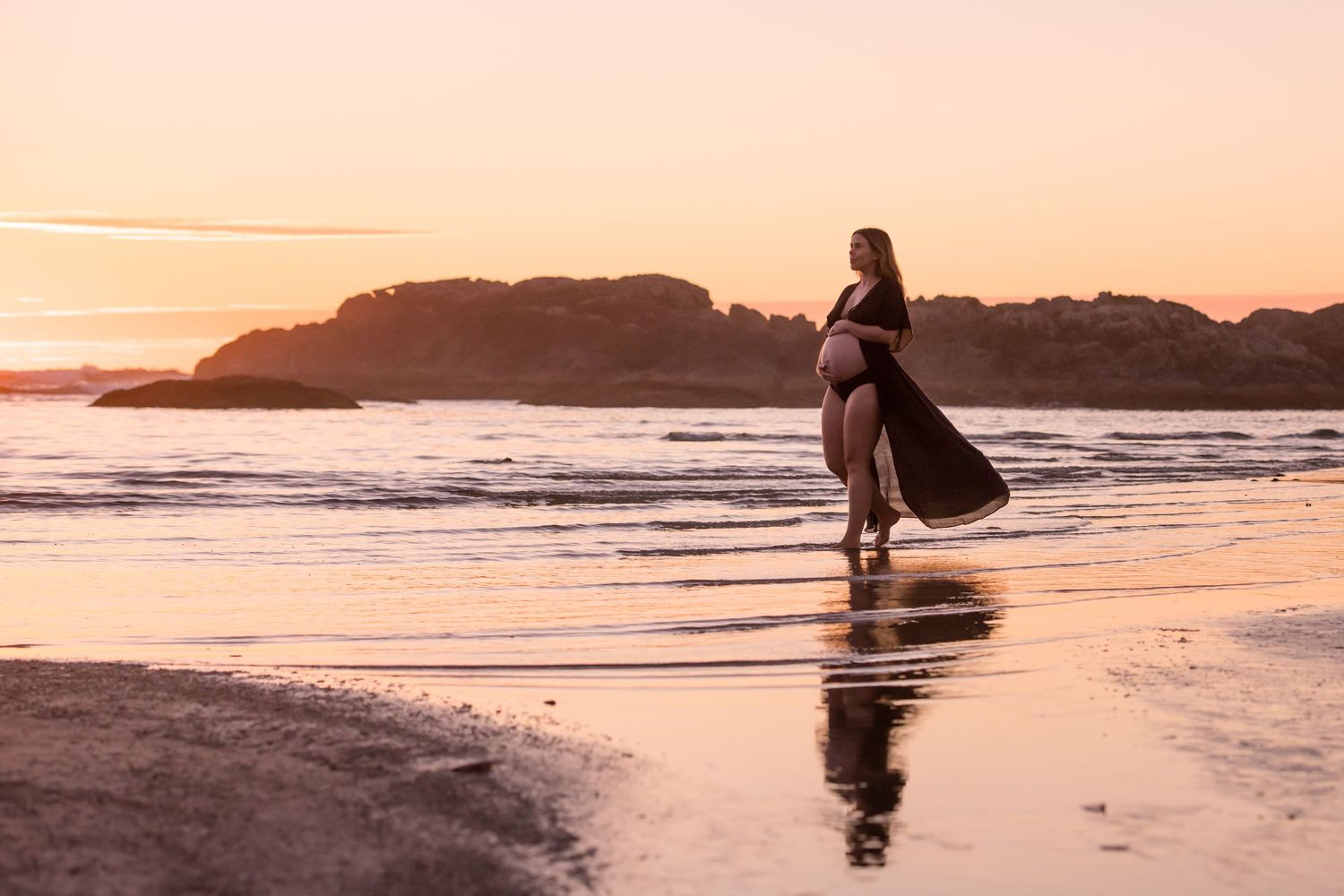 Golden hour beach scene with silhouettes reflected in wet sand during sunset.