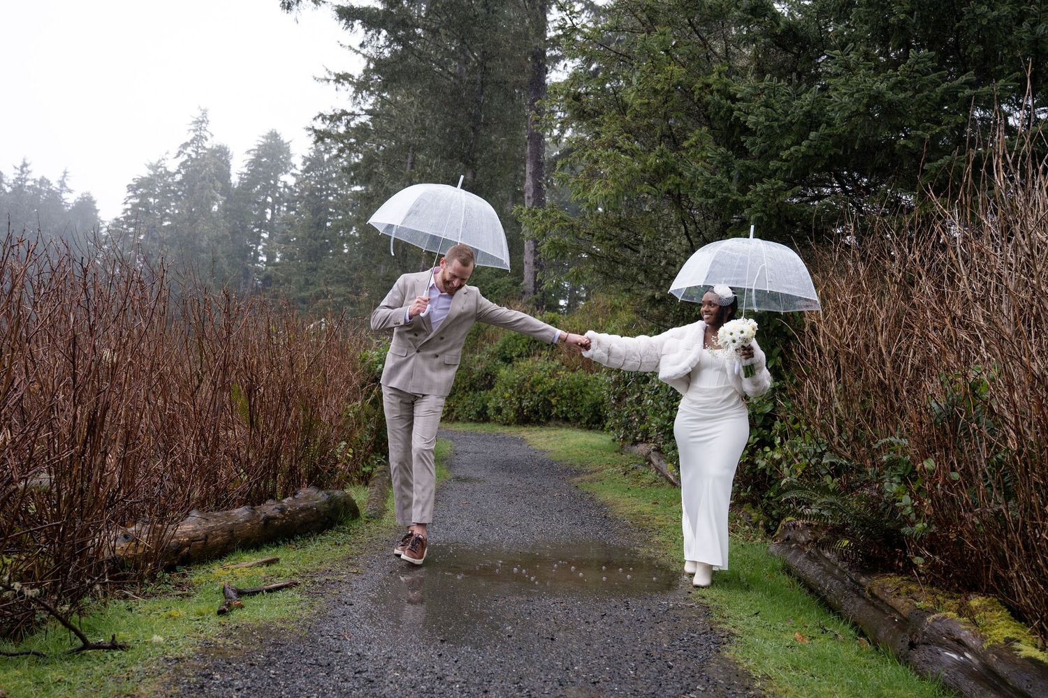 A person in white clothing walks with an umbrella along a misty garden path on a rainy day.