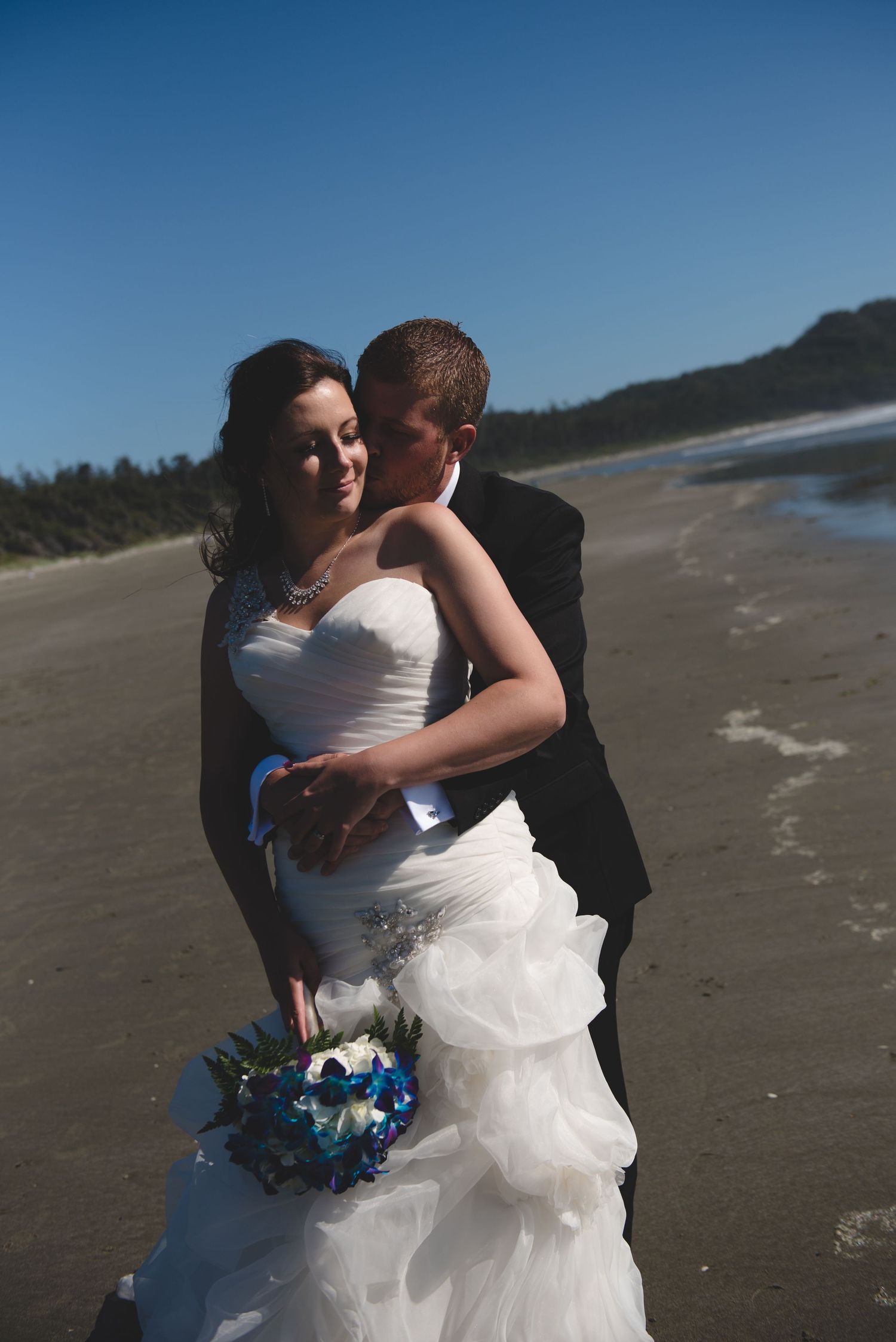 A romantic beach wedding portrait captures an intimate moment between newlyweds at the ocean's edge.