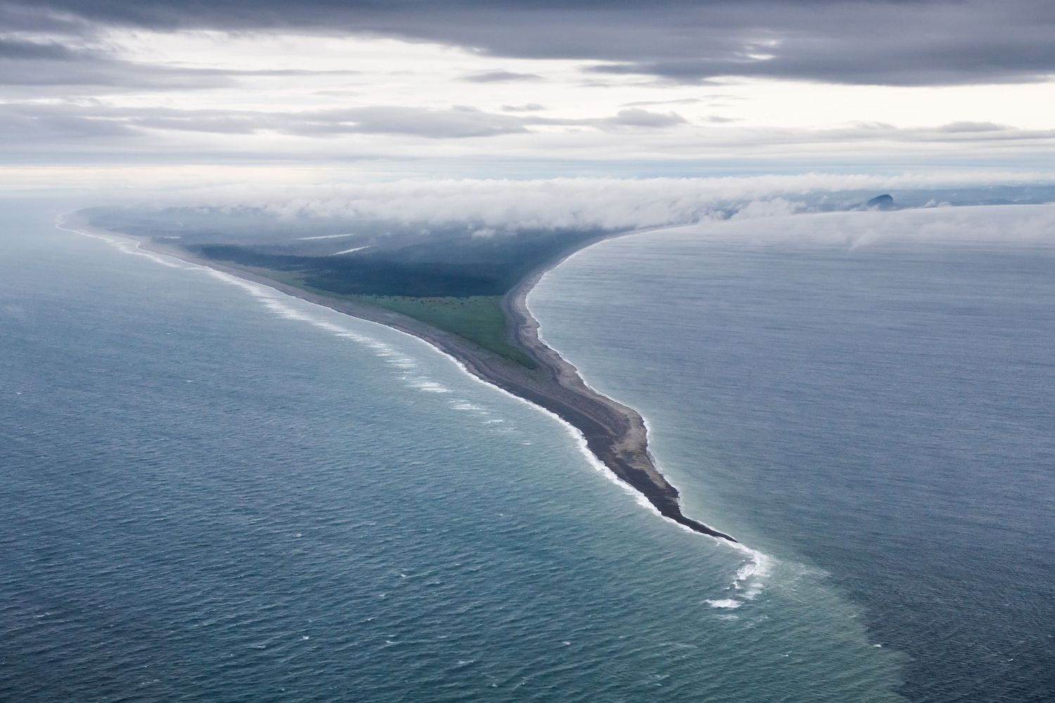 Aerial view of a curved coastline with dramatic cloudy skies over turquoise waters.