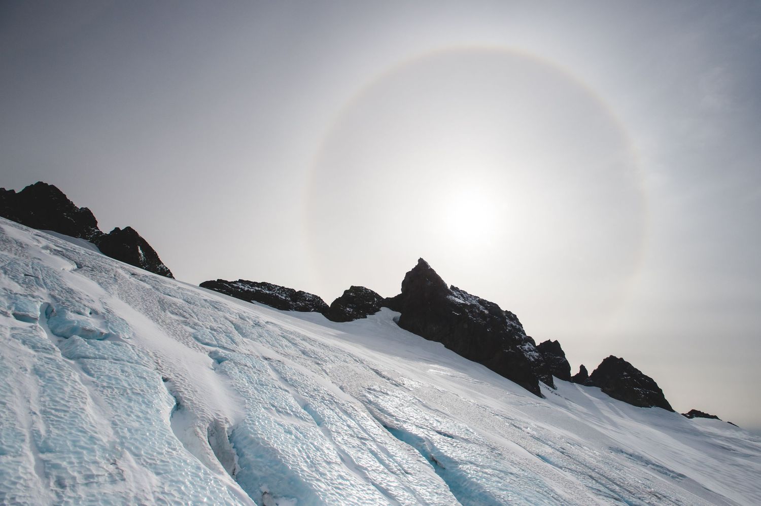 Dramatic sun halo illuminates the snowy mountain landscape with ethereal light.