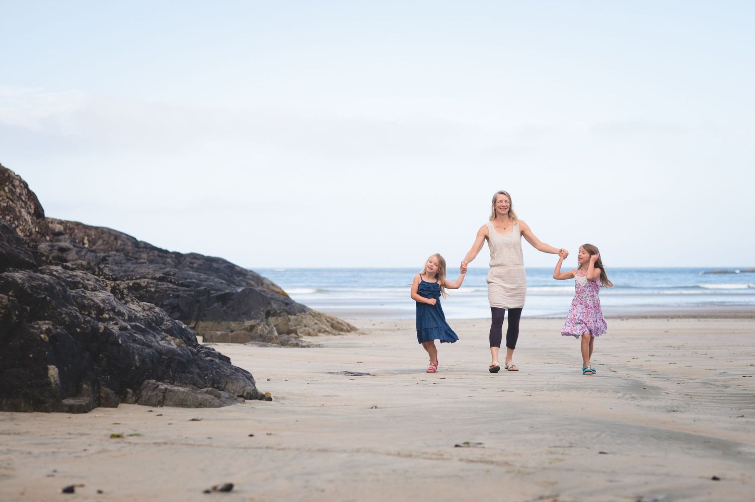 Family walking together and holding hands along a scenic beach shoreline at sunset.