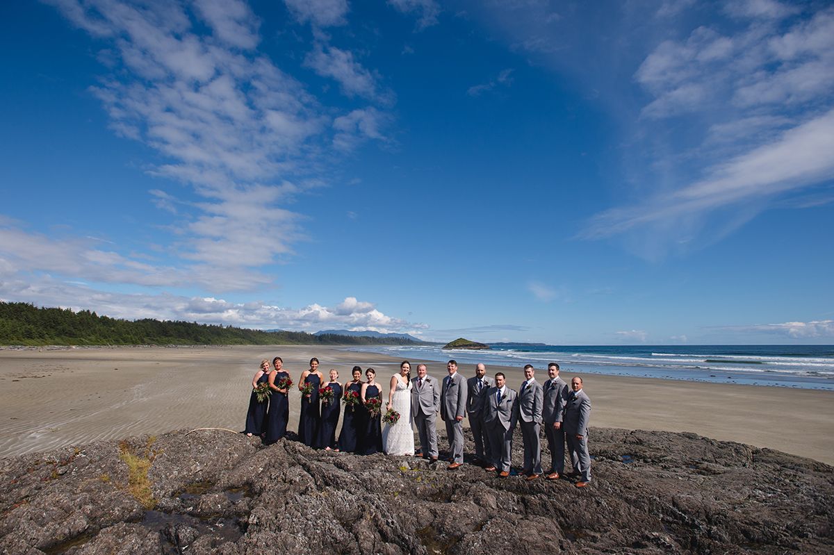 Wedding party lined up against dramatic blue sky and ocean backdrop.