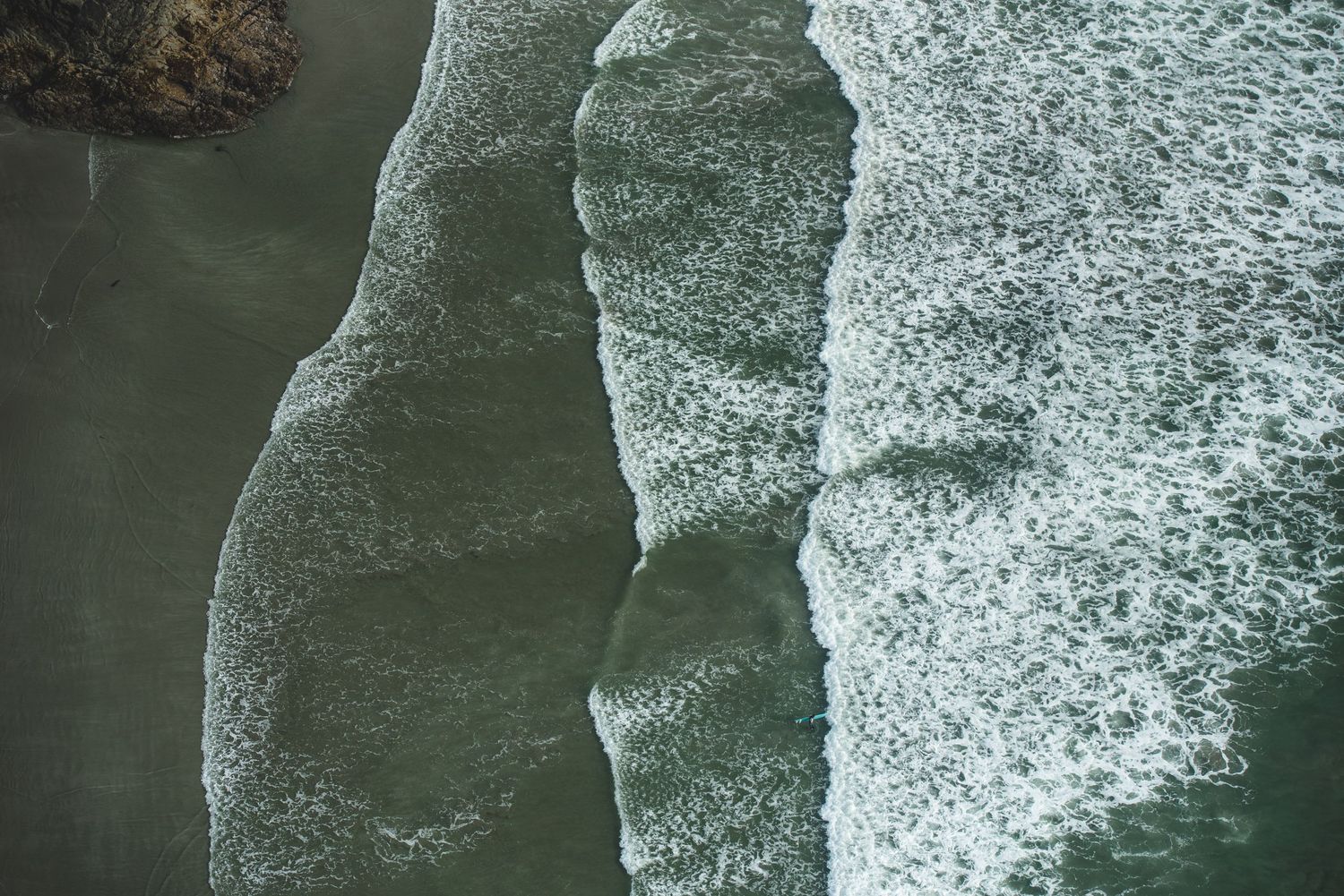 Aerial view of ocean waves creating white foam patterns as they meet the shoreline.