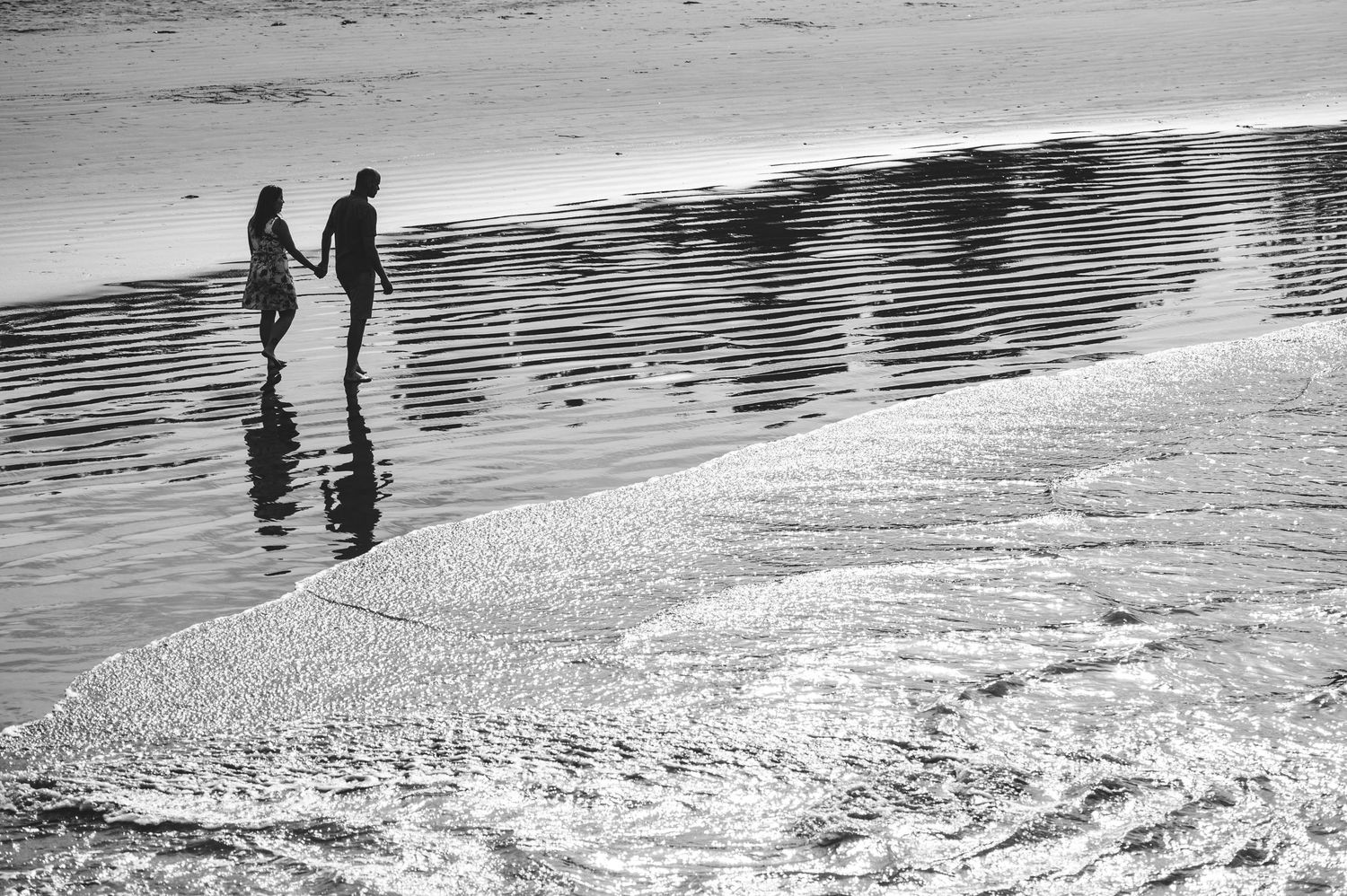 Silhouettes of people walking along a misty shoreline at low tide.