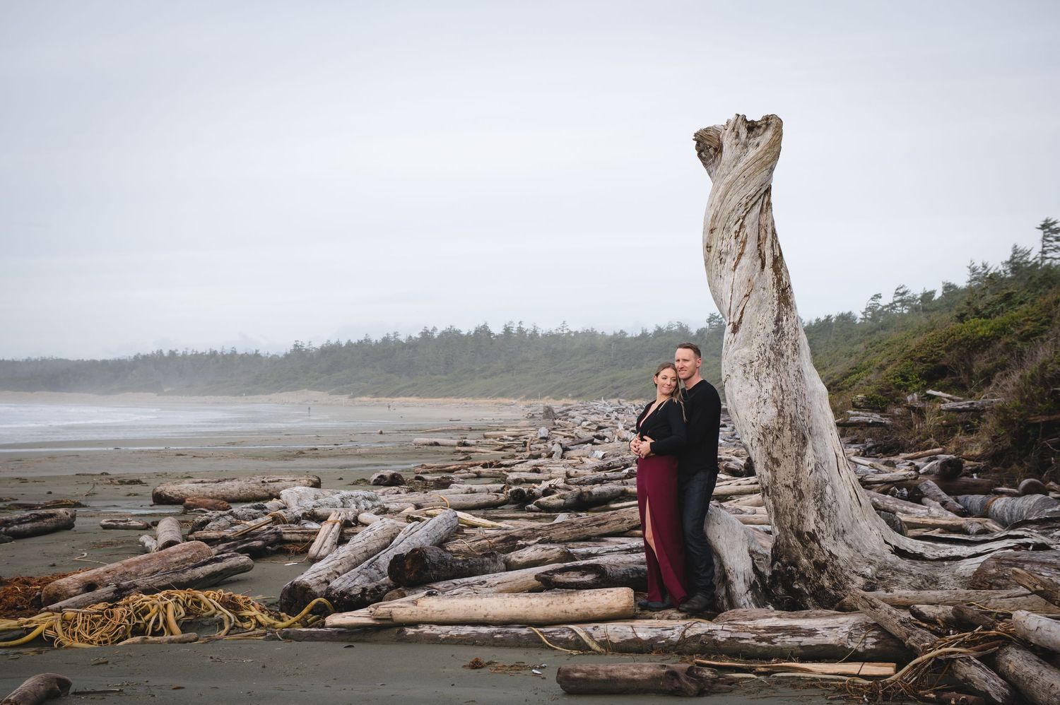 Couple exploring a scenic driftwood-covered Pacific Northwest beach on an overcast day.