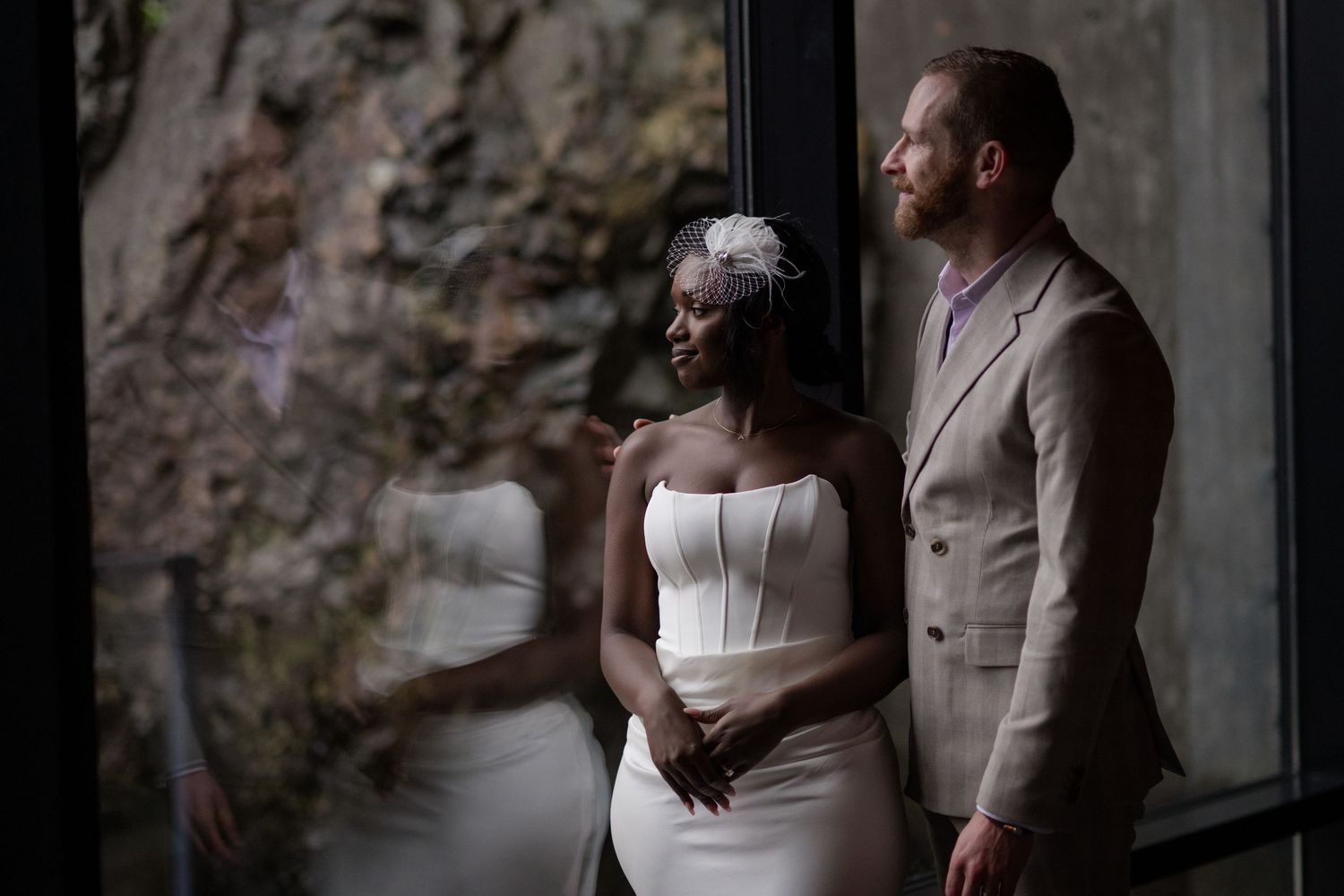 A couple in wedding attire embraces while standing in front of a rustic stone wall.